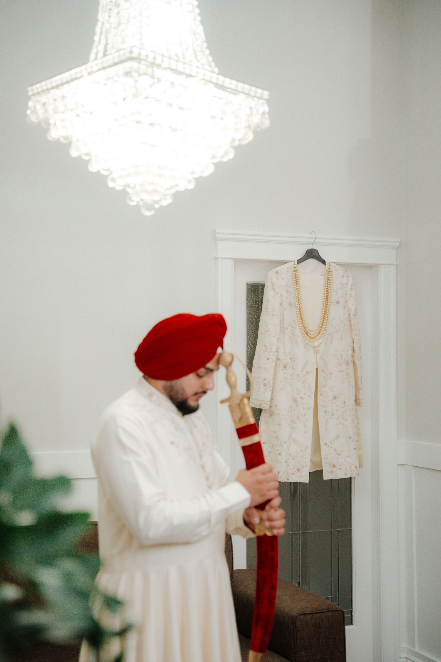Person in white outfit adjusting clothing under crystal chandelier in bright room.