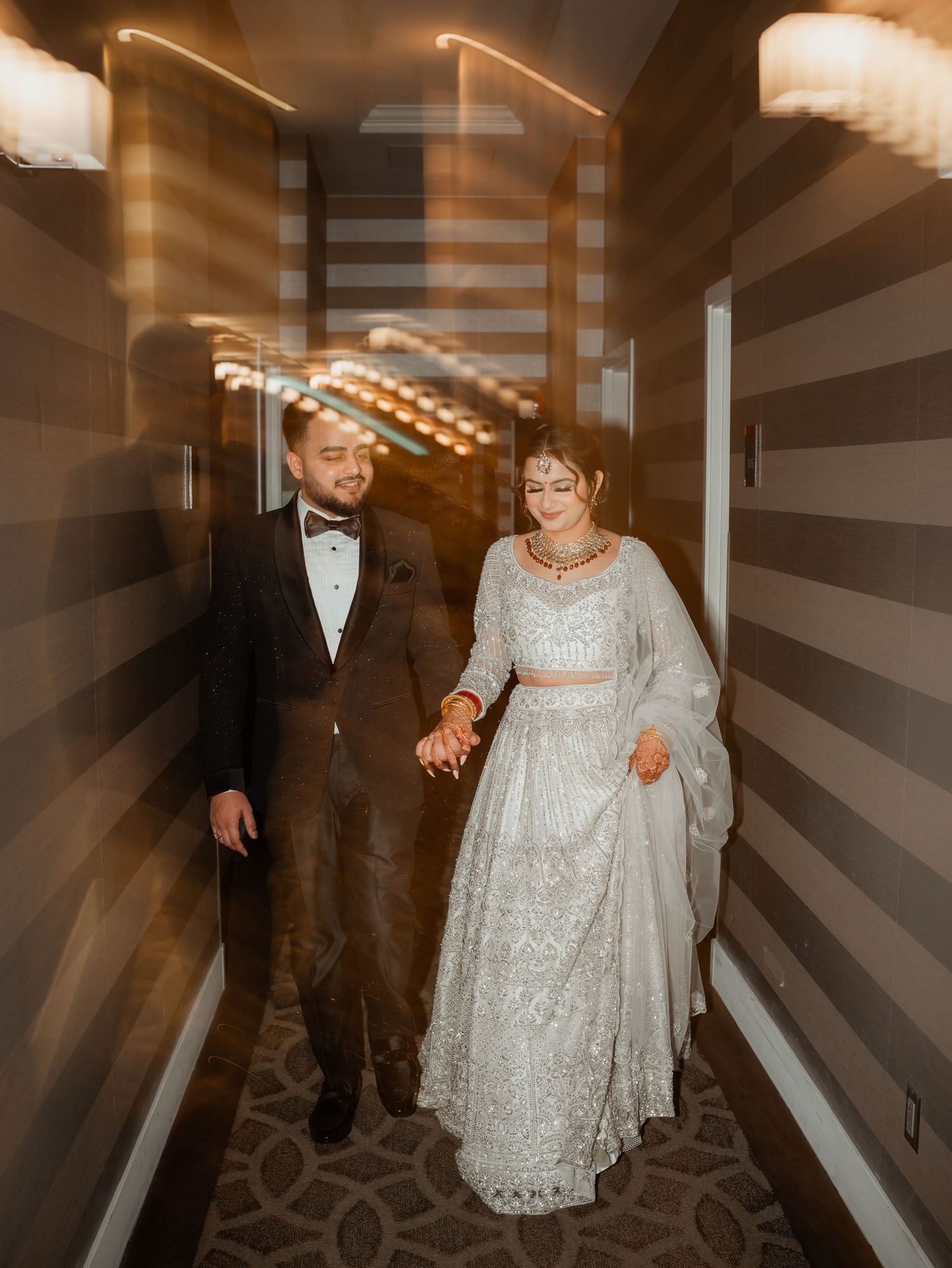 A couple walks down an illuminated corridor with patterned carpeting.