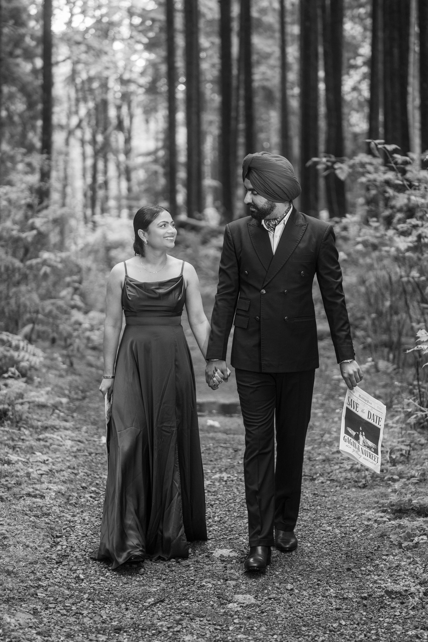 Black and white photo of couple walking hand in hand through a forest path.