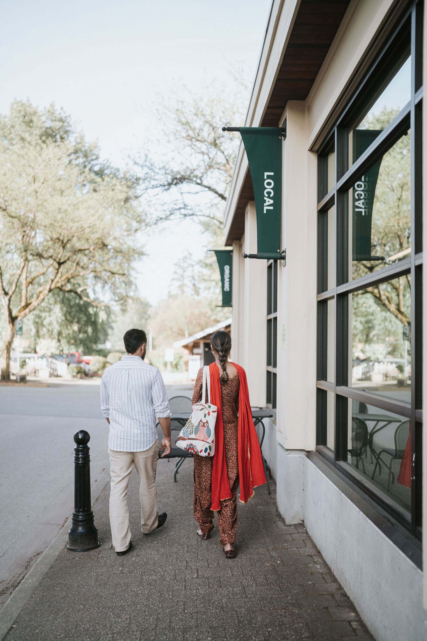 A couple walking along a covered sidewalk with white walls and green awnings on a sunny day.