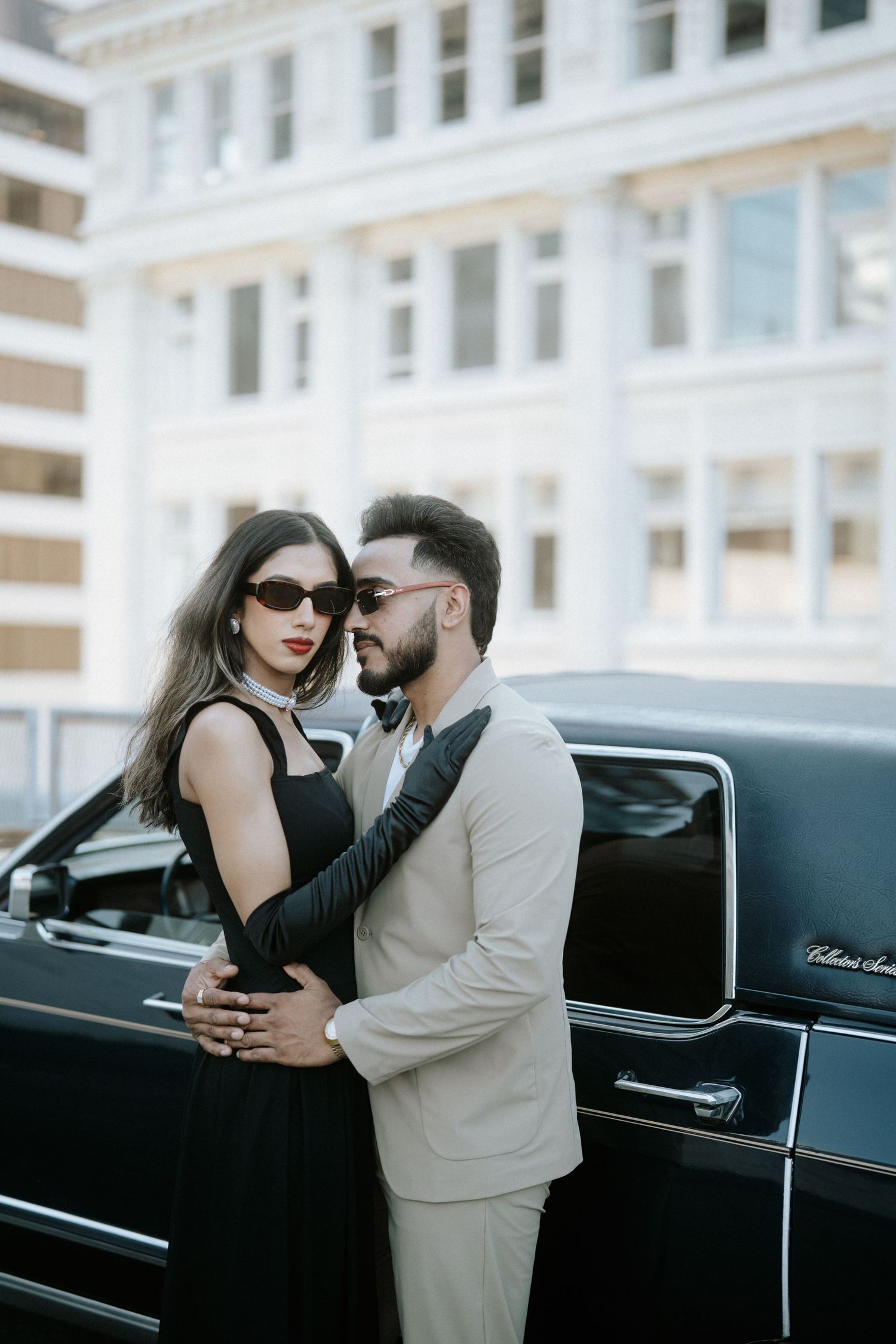 A couple poses romantically against a vintage black car in a series of intimate photos.