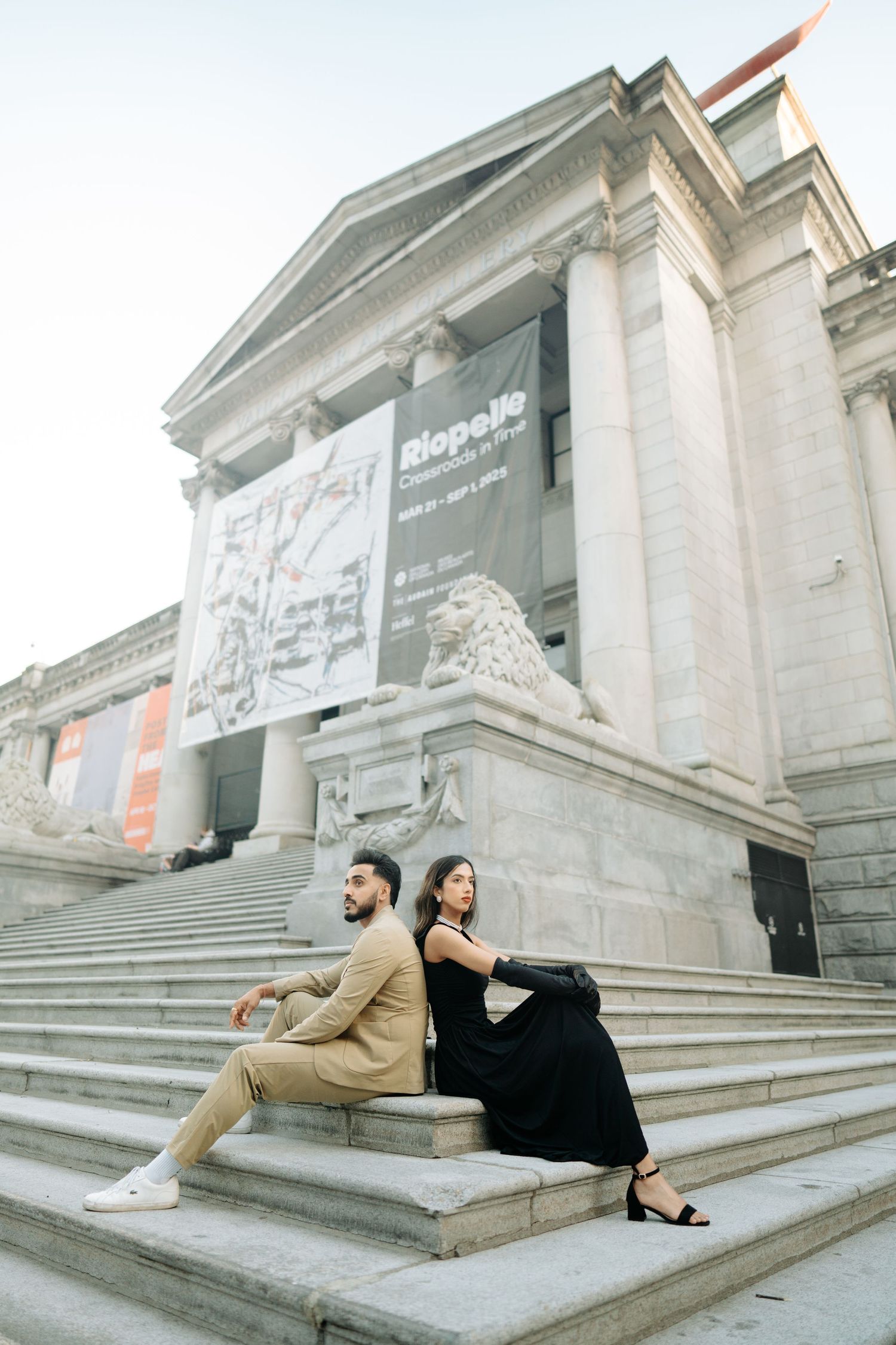Couple sits on stone steps of a grand building in coordinated casual outfits for an urban photoshoot.