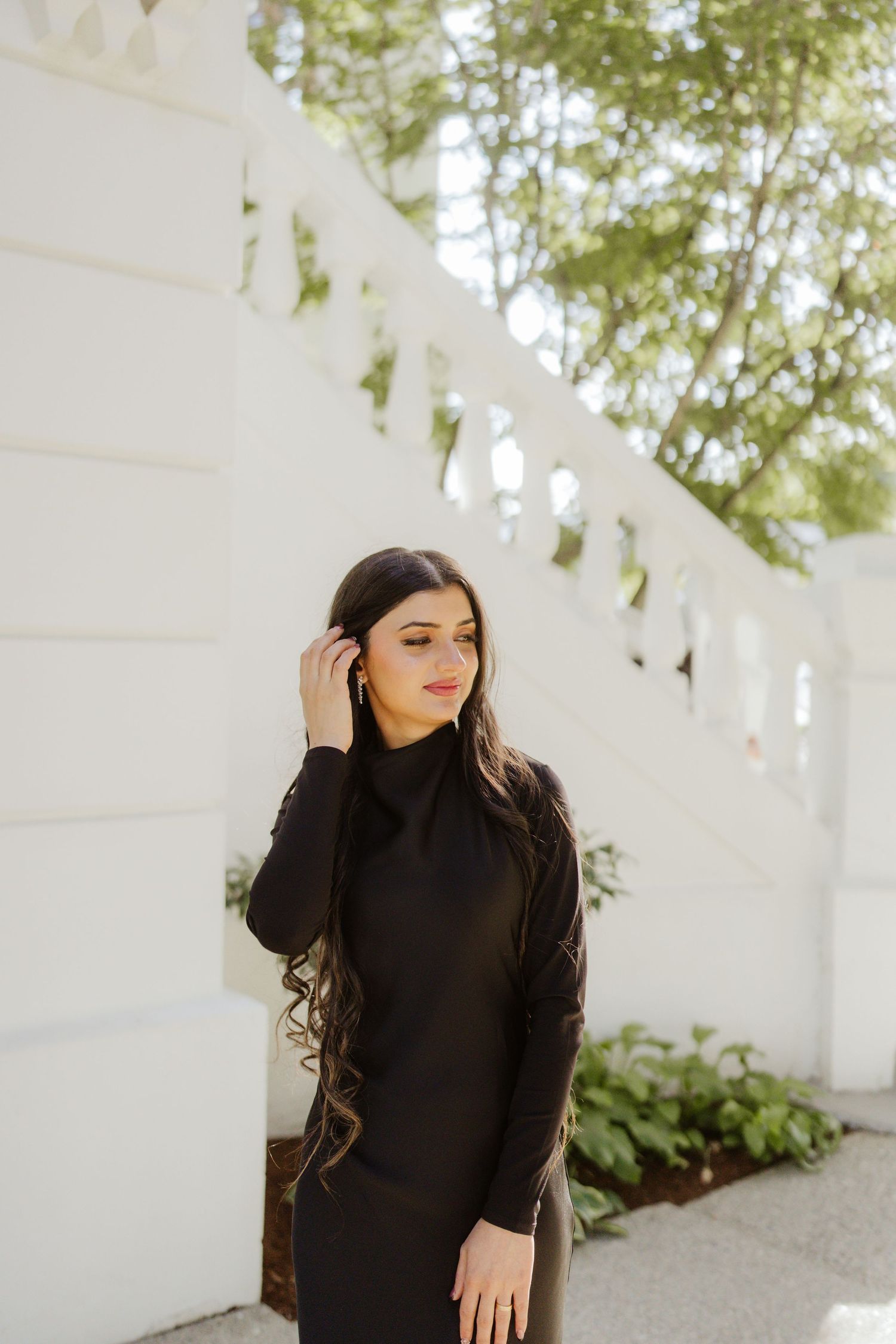 Elegant woman in black turtleneck dress posing beside white decorative balustrade outdoors.