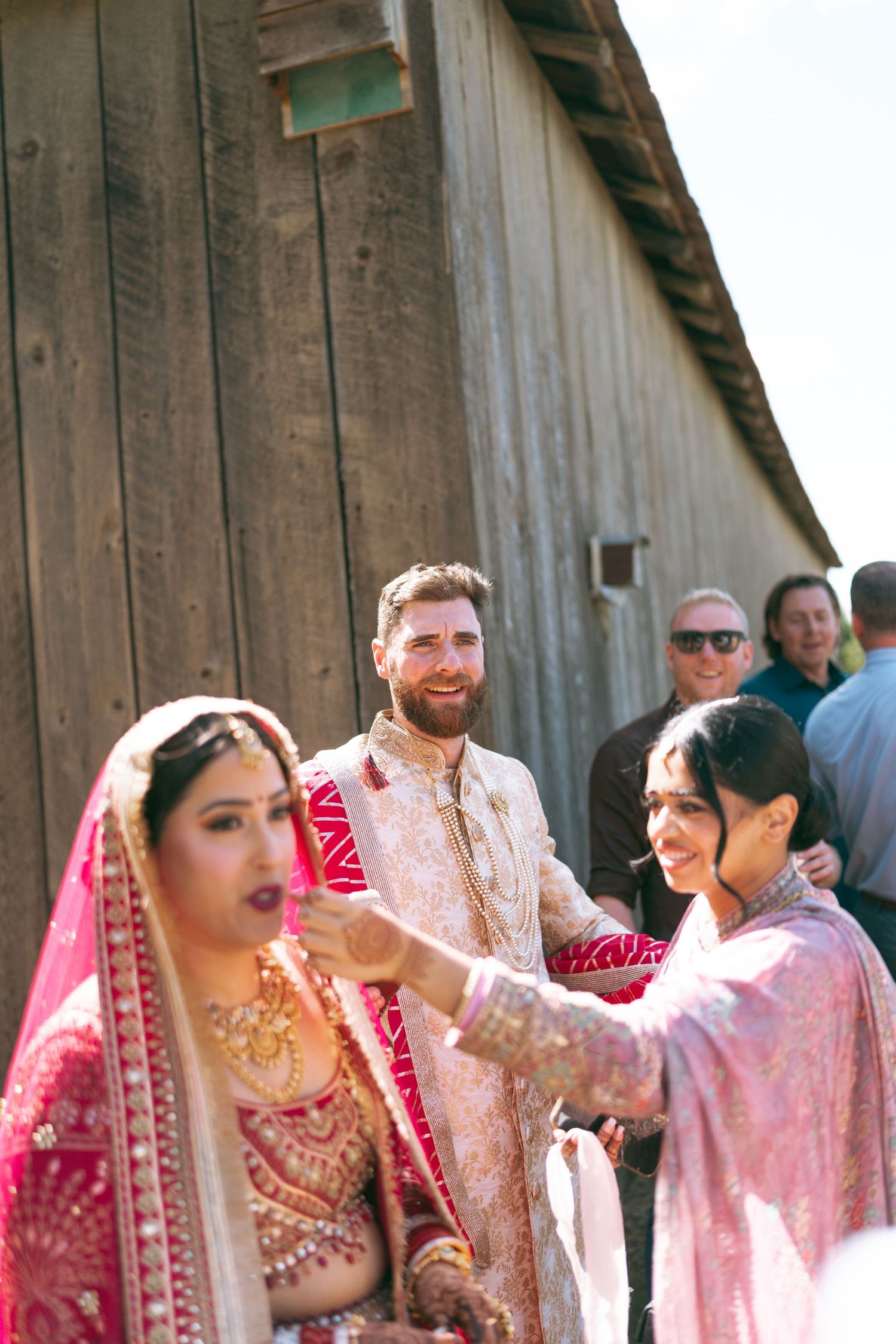 Indian bride in pink lehenga with groom in sherwani during traditional South Asian wedding ceremony outdoors.