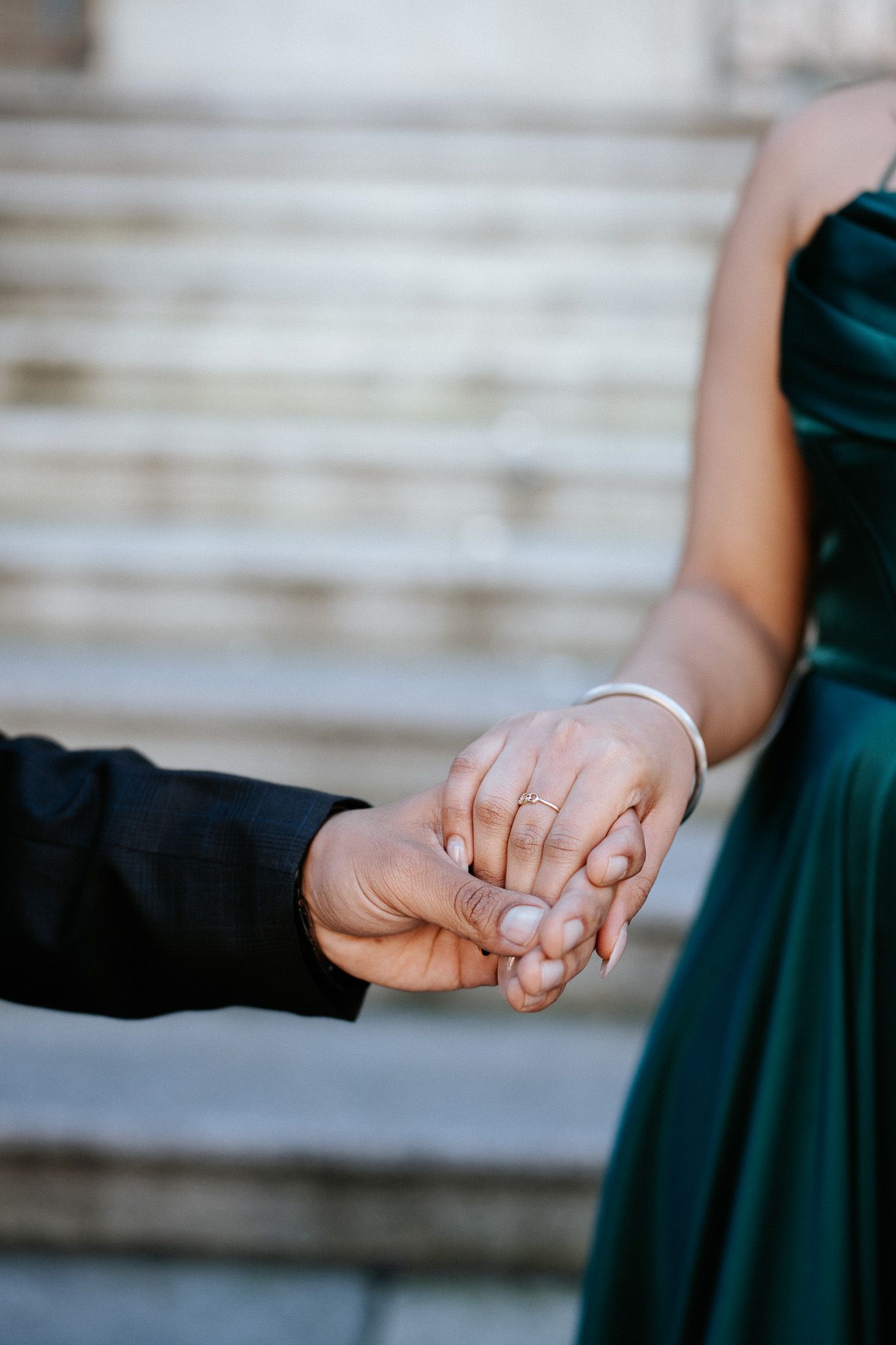 Close-up view of hands holding each other with engagement rings against a blurred background.