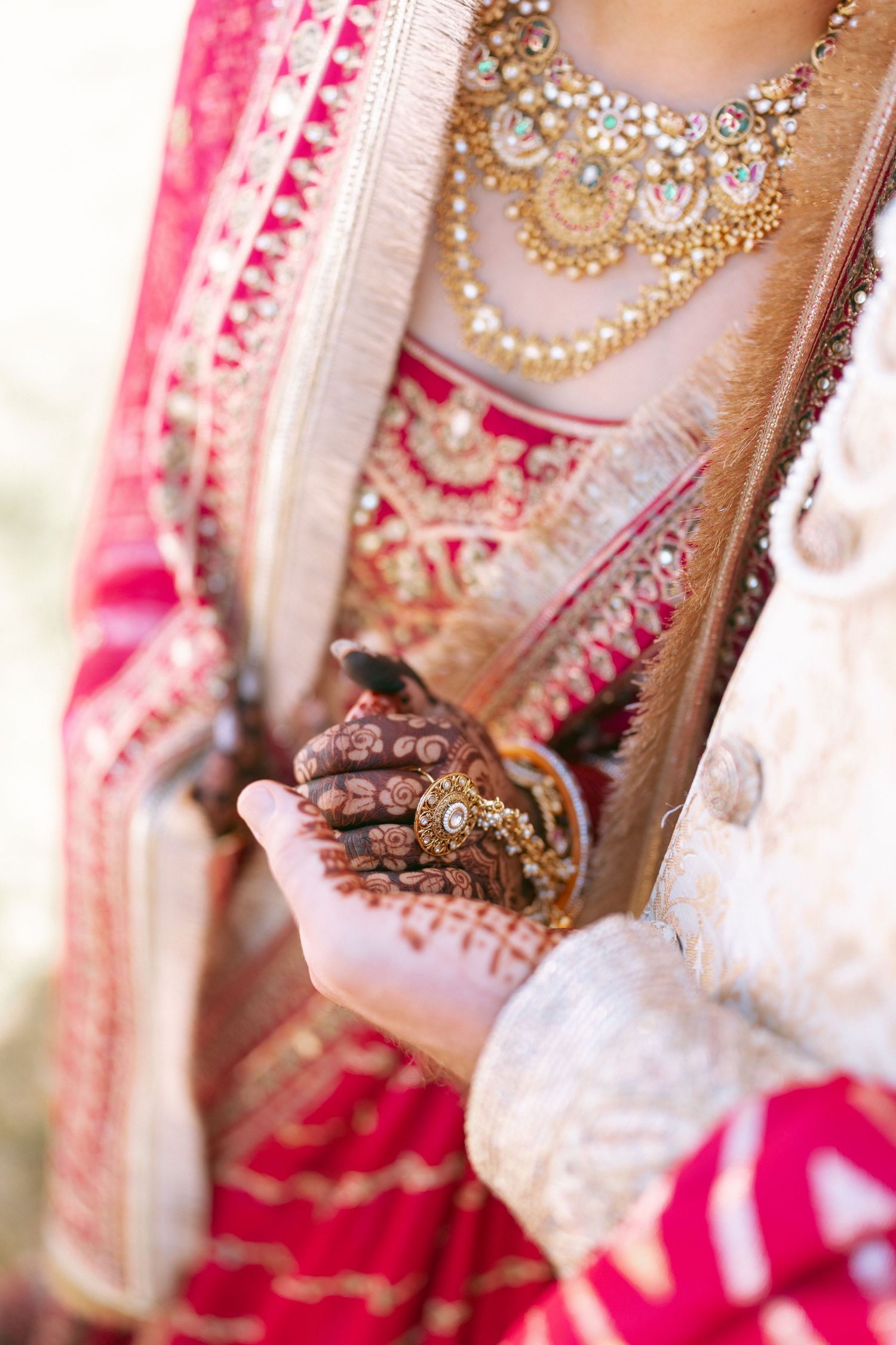 Indian bride in red saree with gold jewelry and mehndi hands held by groom during traditional wedding ceremony.