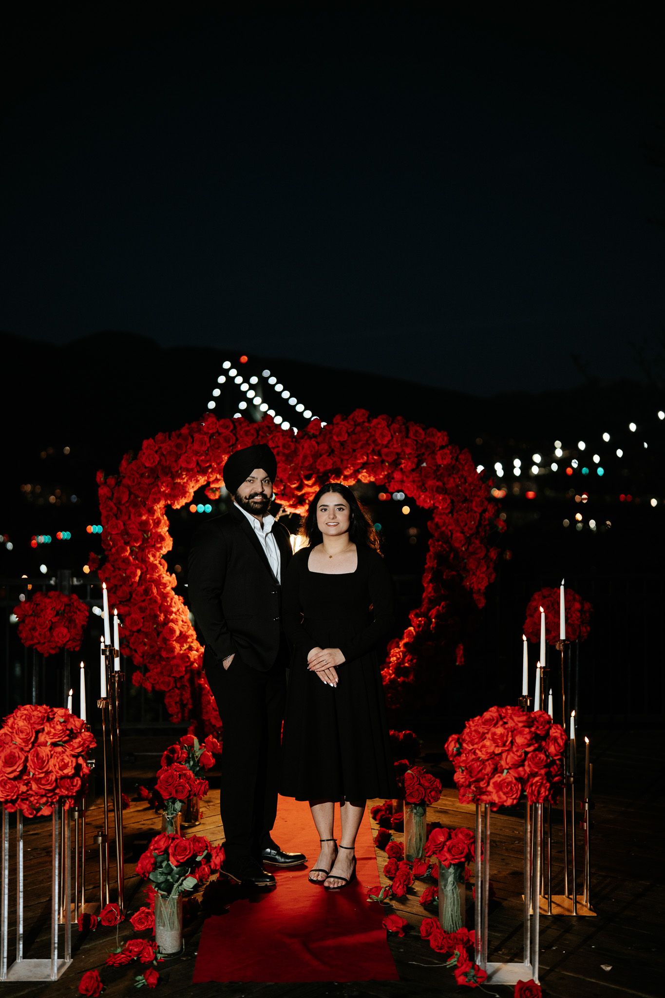 A romantic nighttime garden setting with illuminated red floral arches and string lights creating a magical atmosphere.