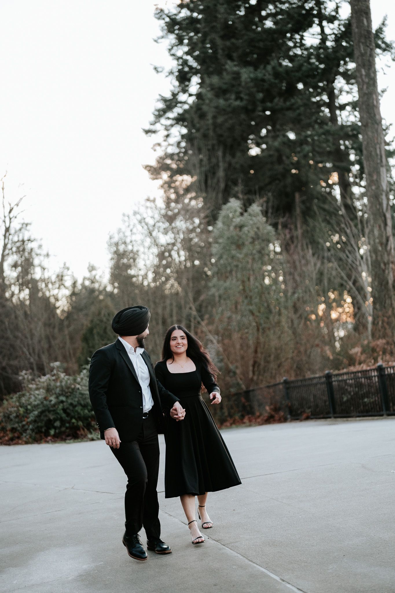 A couple in formal attire dances together on a concrete patio surrounded by trees at dusk.