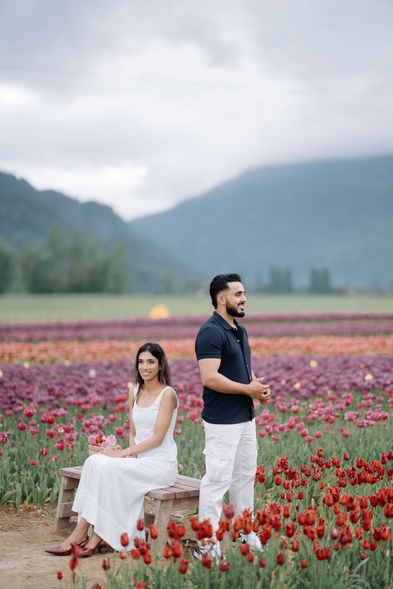 Couple poses romantically in a vibrant red tulip field with misty mountains in the background.