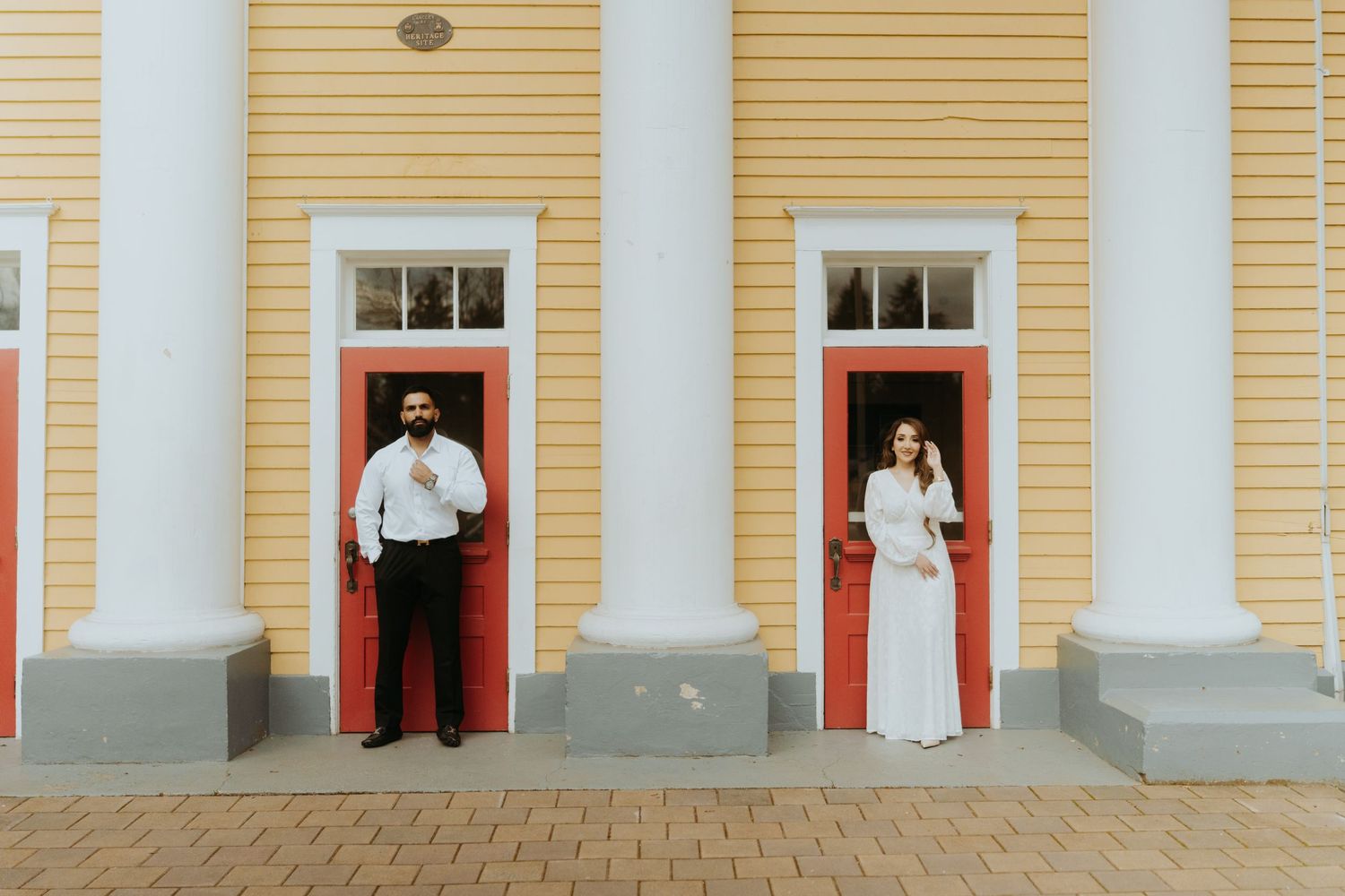 Symmetrical view of a yellow colonial building with white columns and red doors.