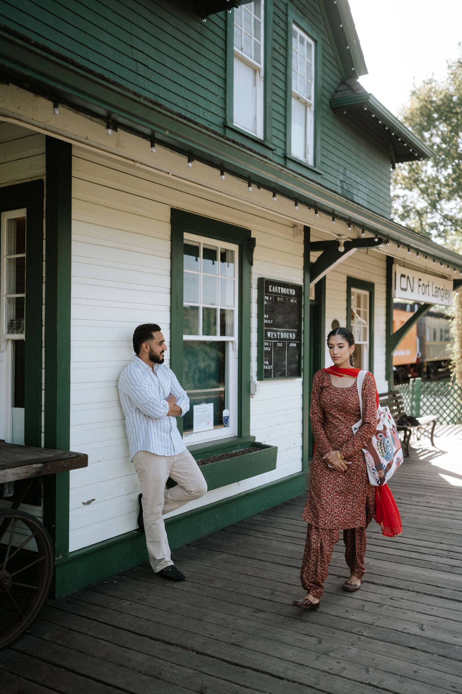 People walk along a covered wooden porch with white walls and green trim on a historic building.
