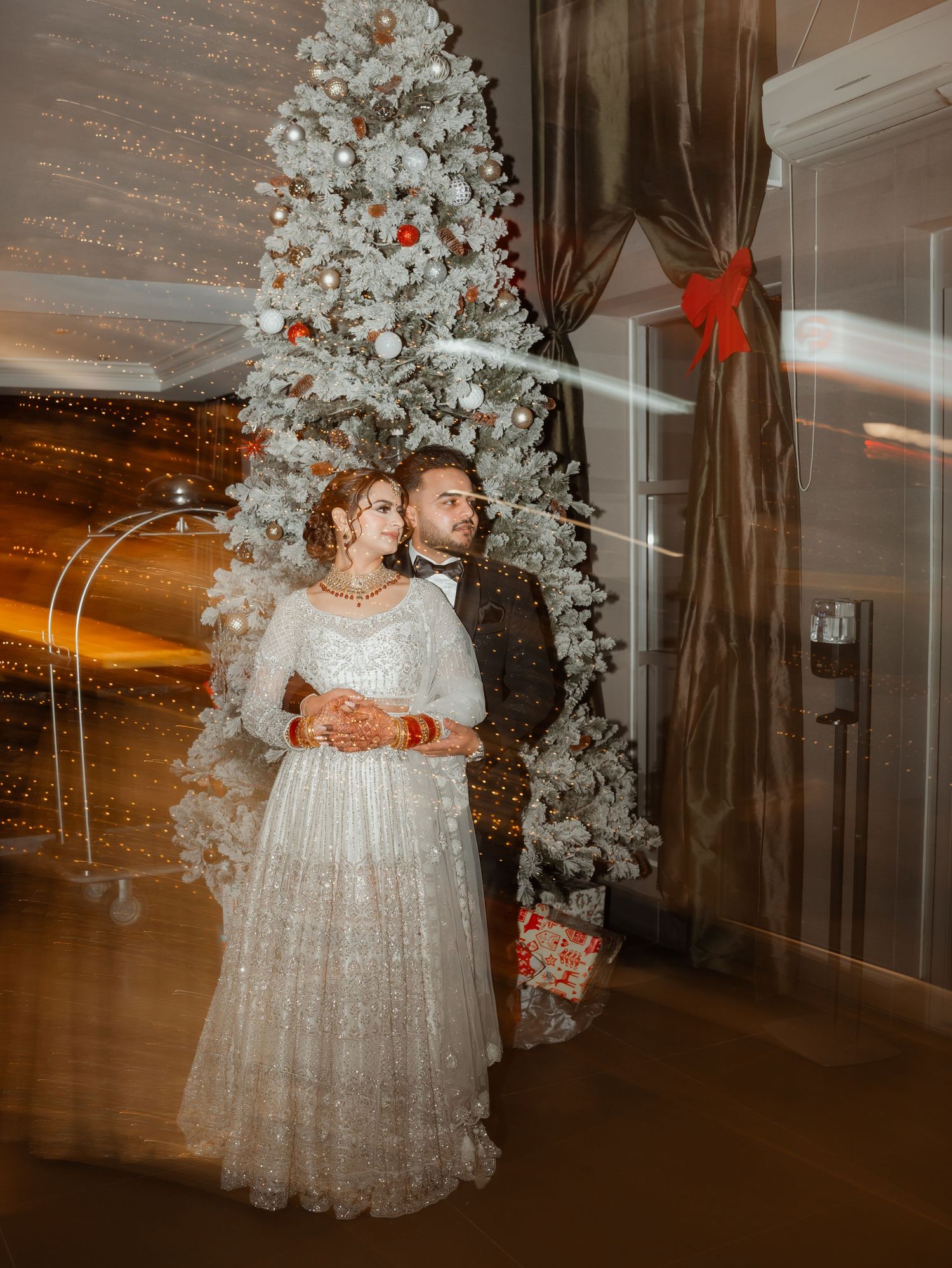 A couple poses near white floral arrangements in an elegantly decorated reception venue.