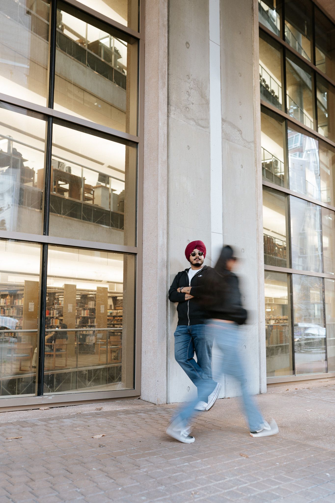 A blurred motion sequence shows a person walking past a modern building facade with large windows and concrete columns.