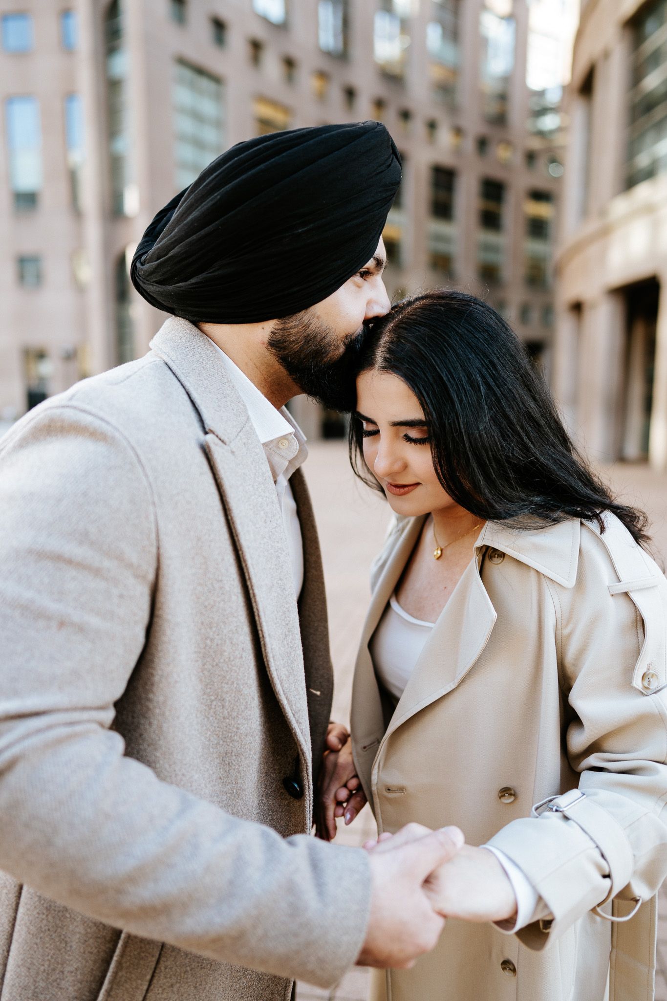 A couple in matching beige coats share an intimate moment together in an urban setting.
