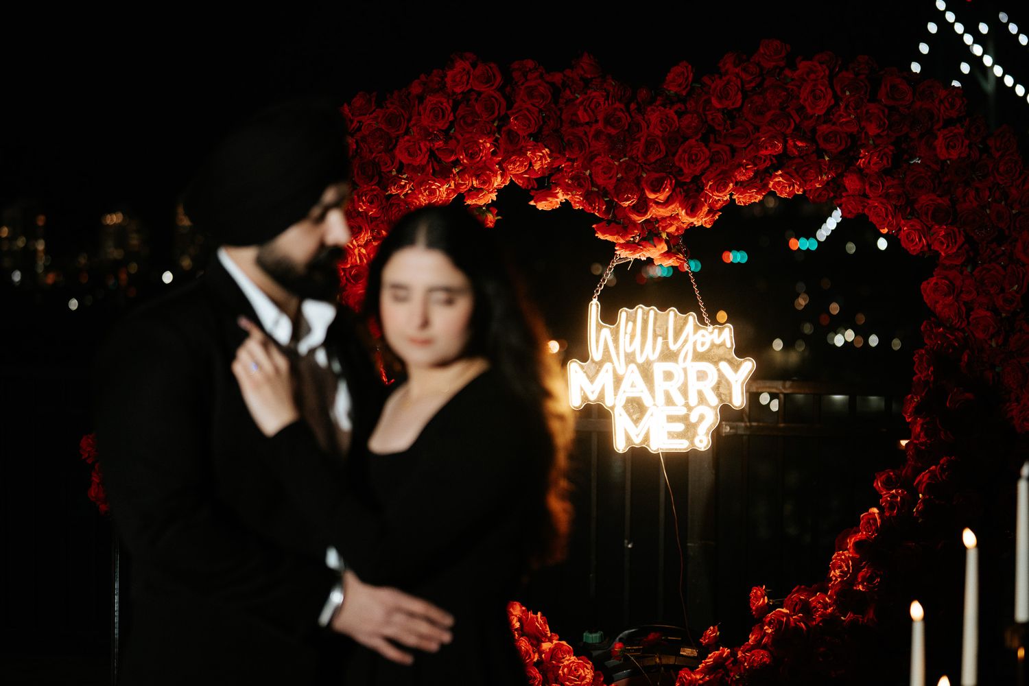 A couple embraces while dancing beneath a crystal chandelier with red floral decorations at an elegant event.