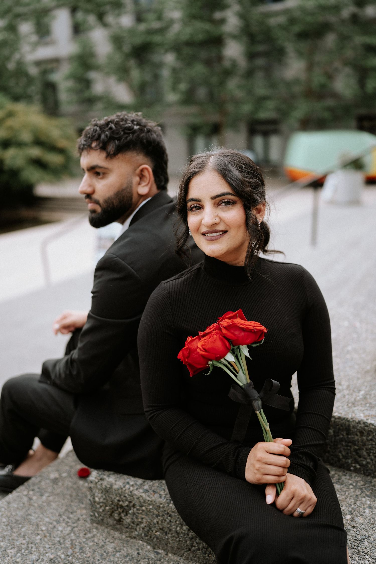Couple in matching black outfits shares candid moments with red roses outdoors.