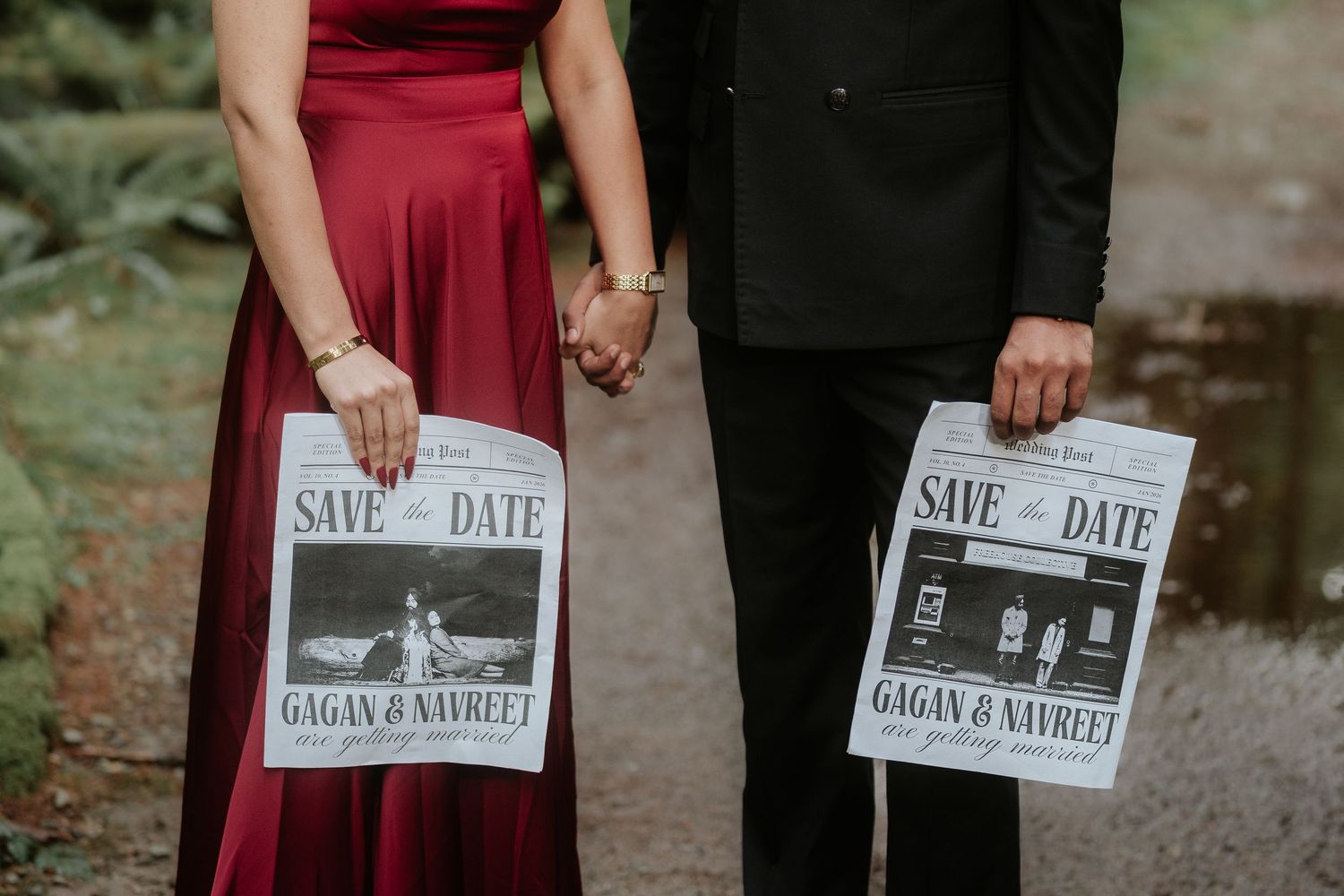 Couple in formal attire holds matching save the date announcements while standing in a forest.