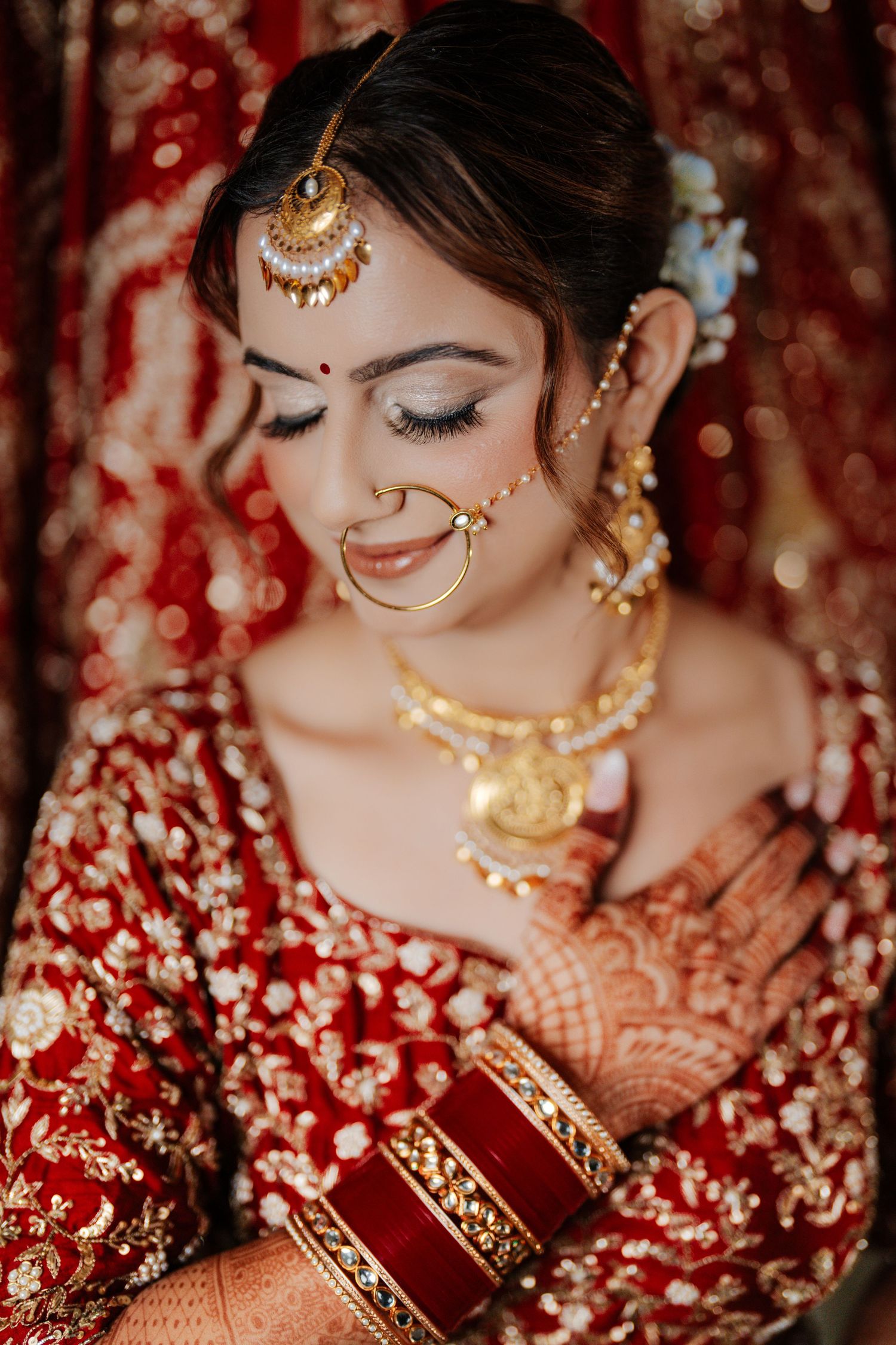 Close-up details of traditional Indian bridal jewelry and mehndi adorned hands with red and gold accents.
