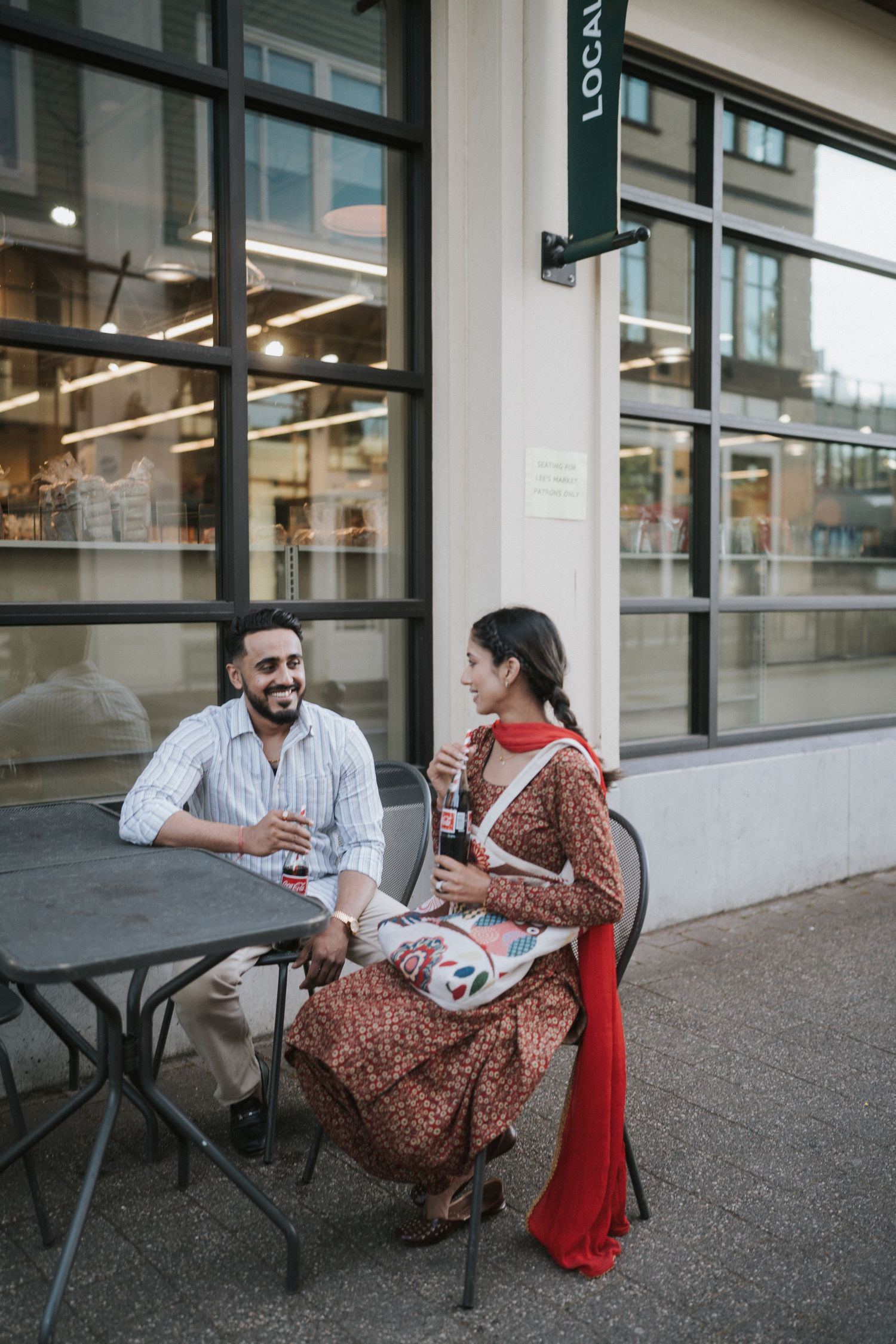 Two people sitting at an outdoor table having a conversation and laughing together at a storefront.