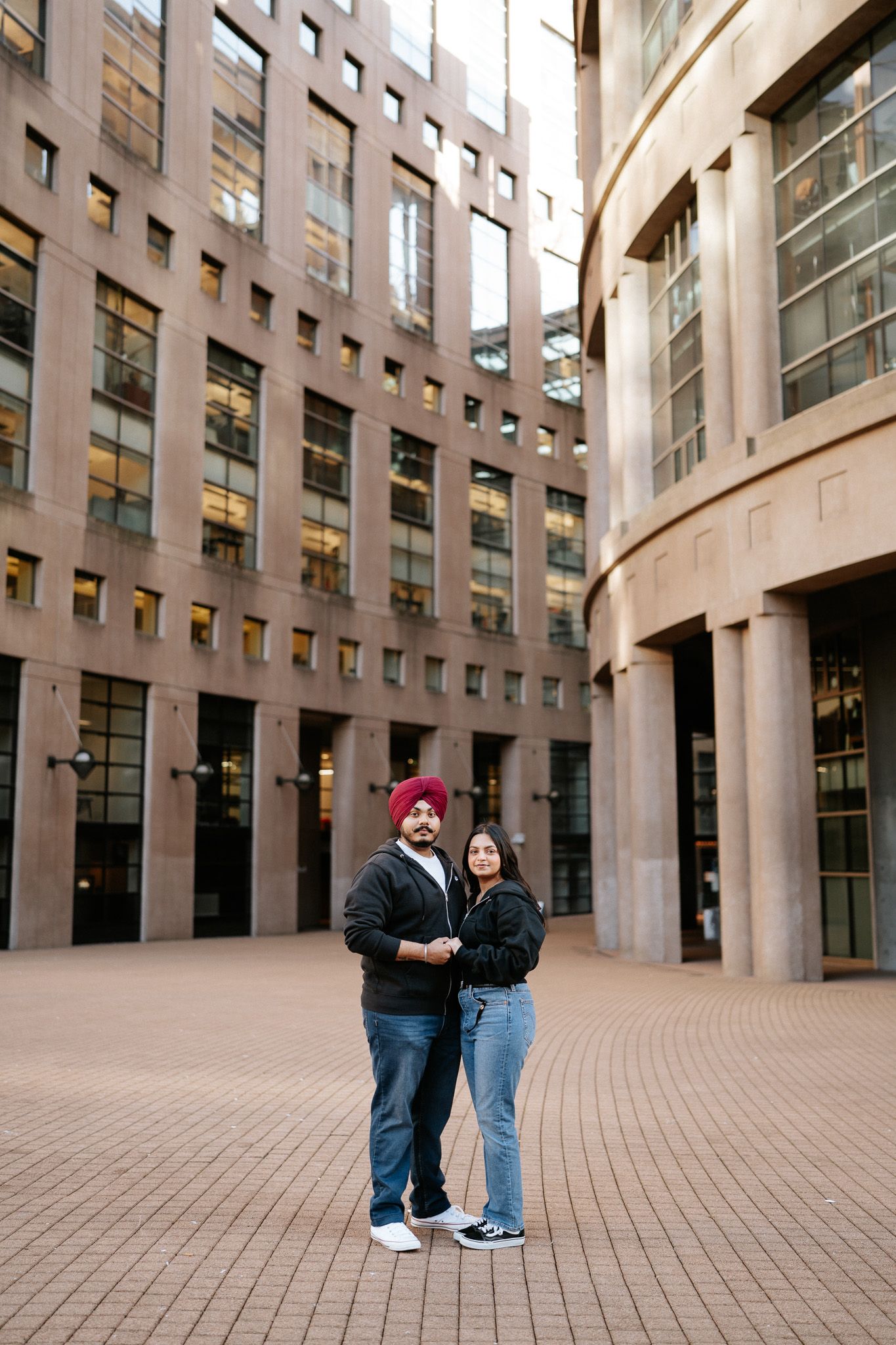A couple stands together in a curved architectural courtyard surrounded by modern office buildings.