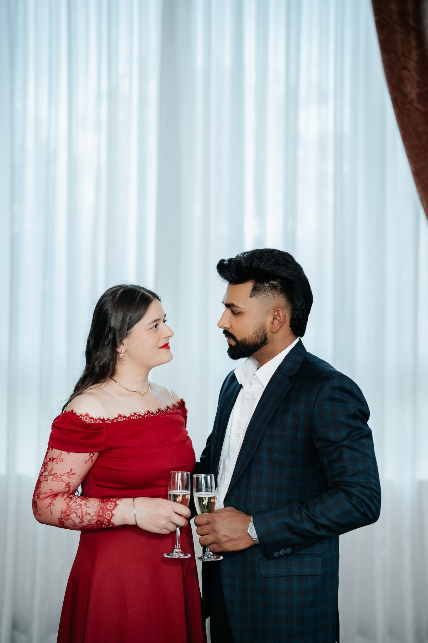 Elegant couple in formal attire toasting with champagne glasses, woman in red dress and man in plaid suit.
