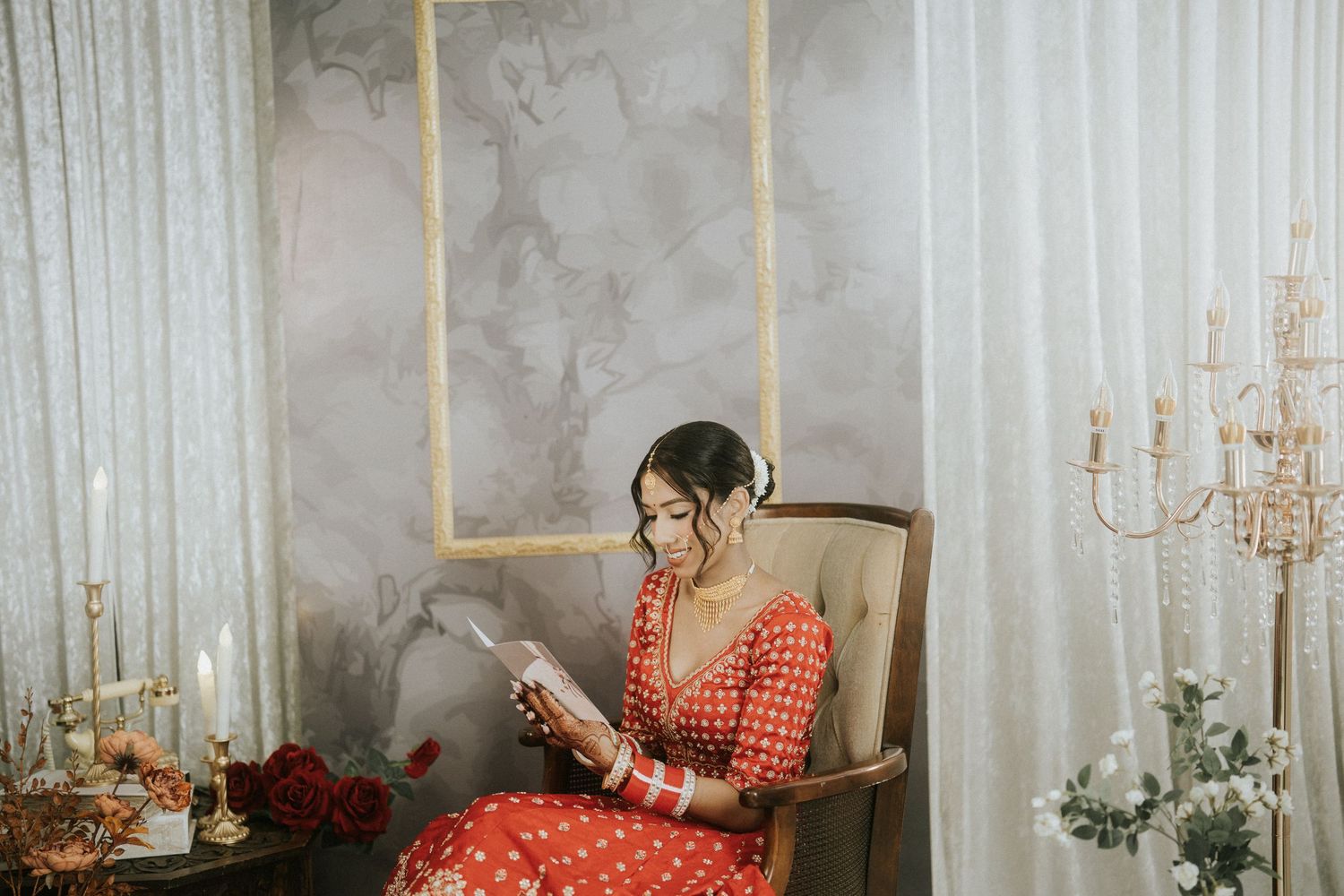 Candlelit room with elegant decor featuring a bride in traditional red attire reading personal notes.