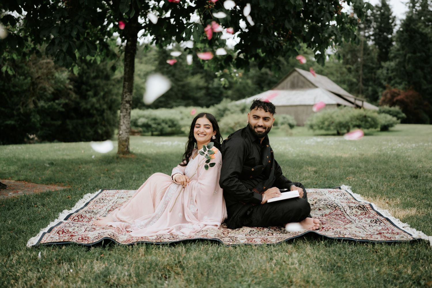 A couple's photoshoot in a park setting with floating rose petals and a patterned blanket.
