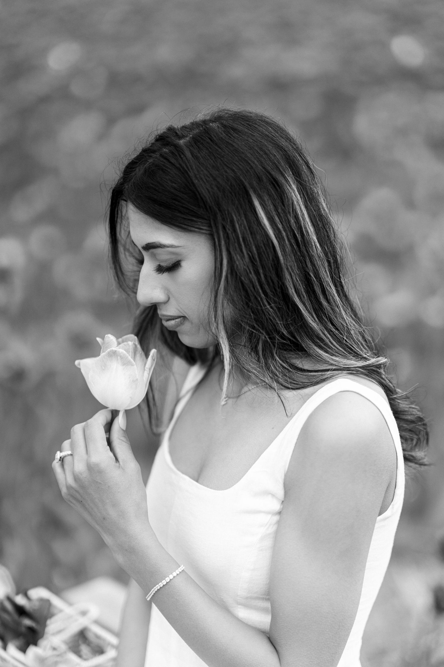 A series of black and white photos showing a woman in a white tank top holding and smelling a flower in nature.
