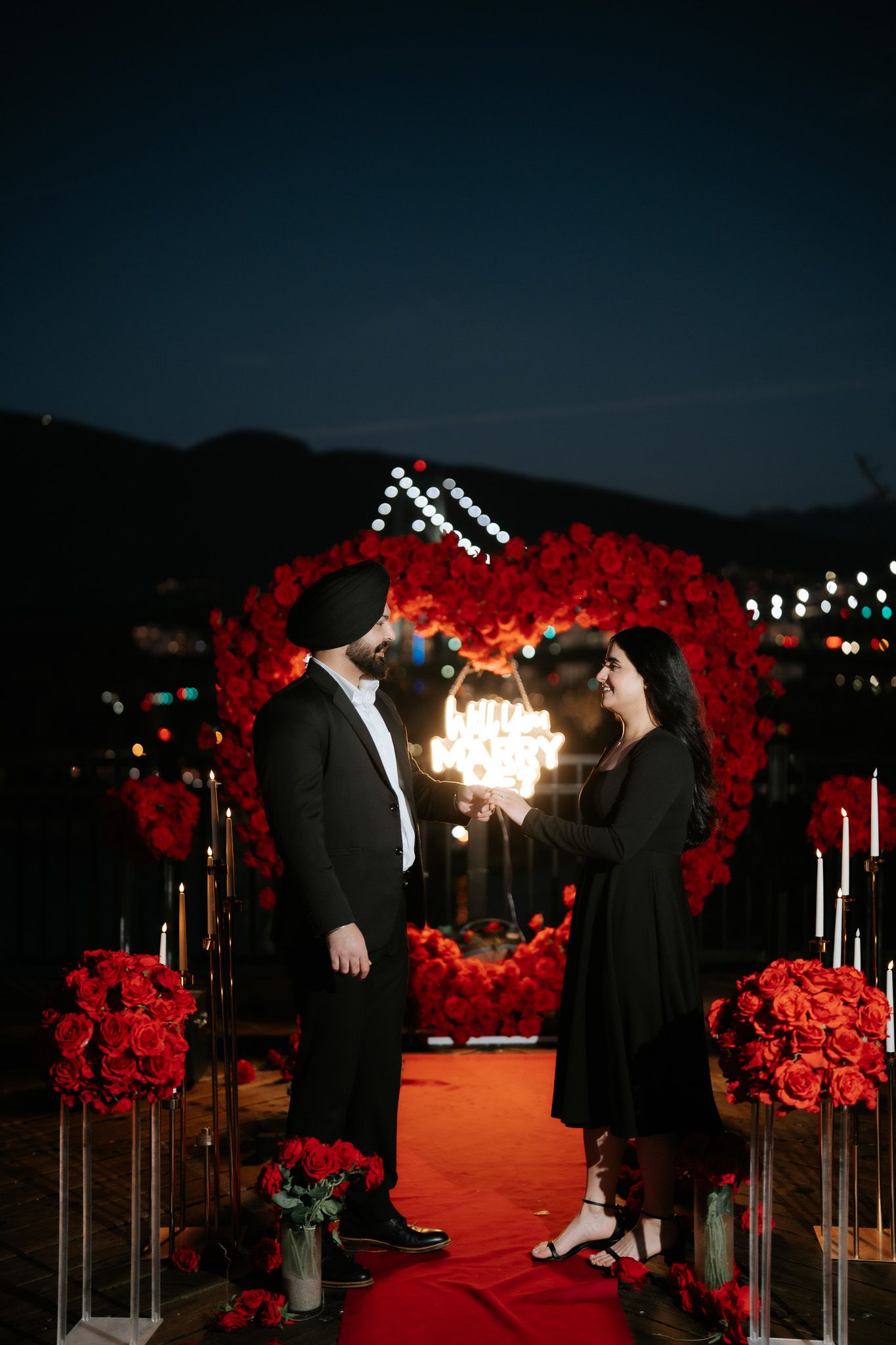A romantic proposal scene at night with a red rose-lined walkway and glowing lights creating an intimate atmosphere.