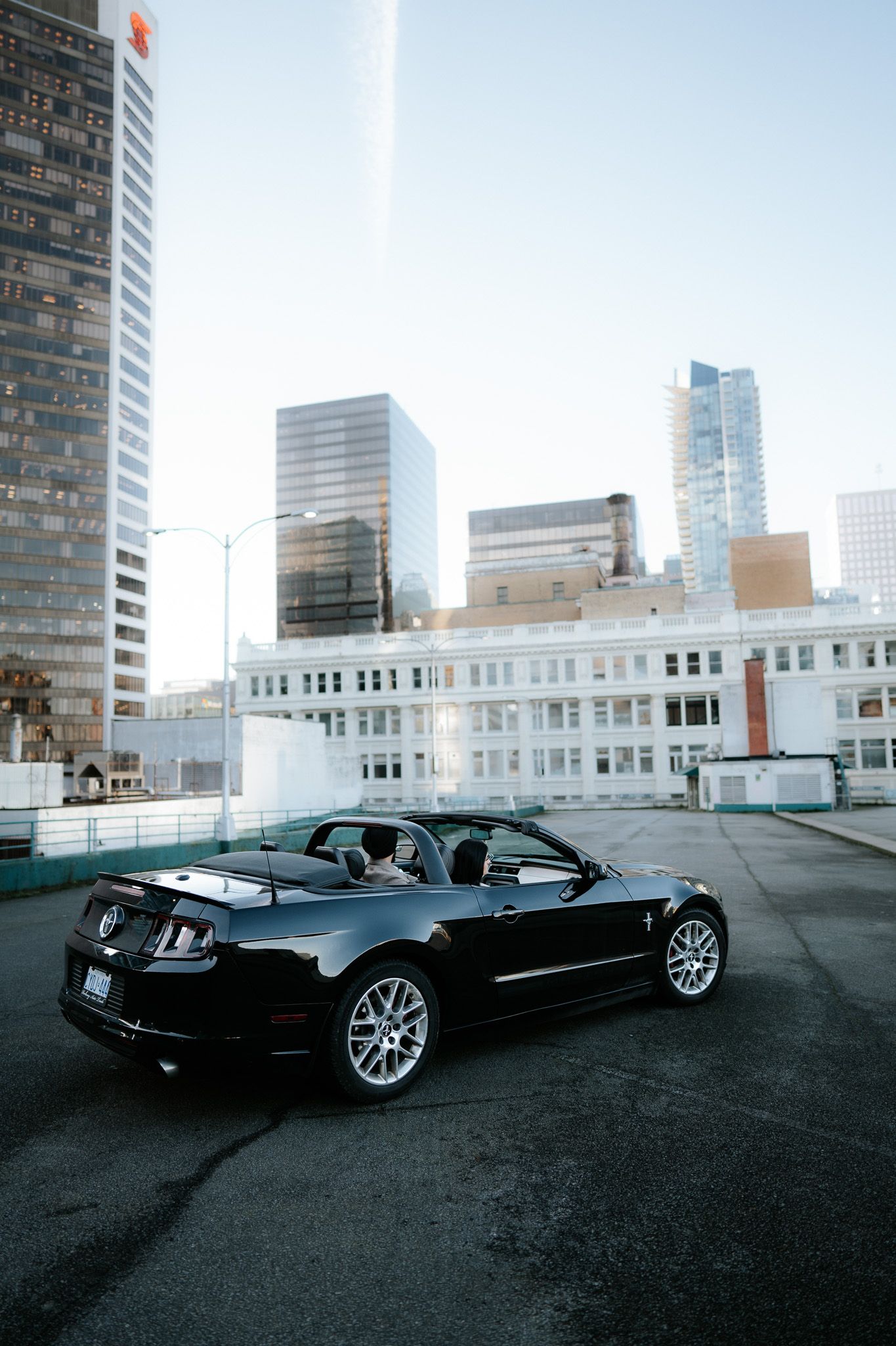A sleek black convertible car photographed from different angles in a city parking lot with skyscrapers.
