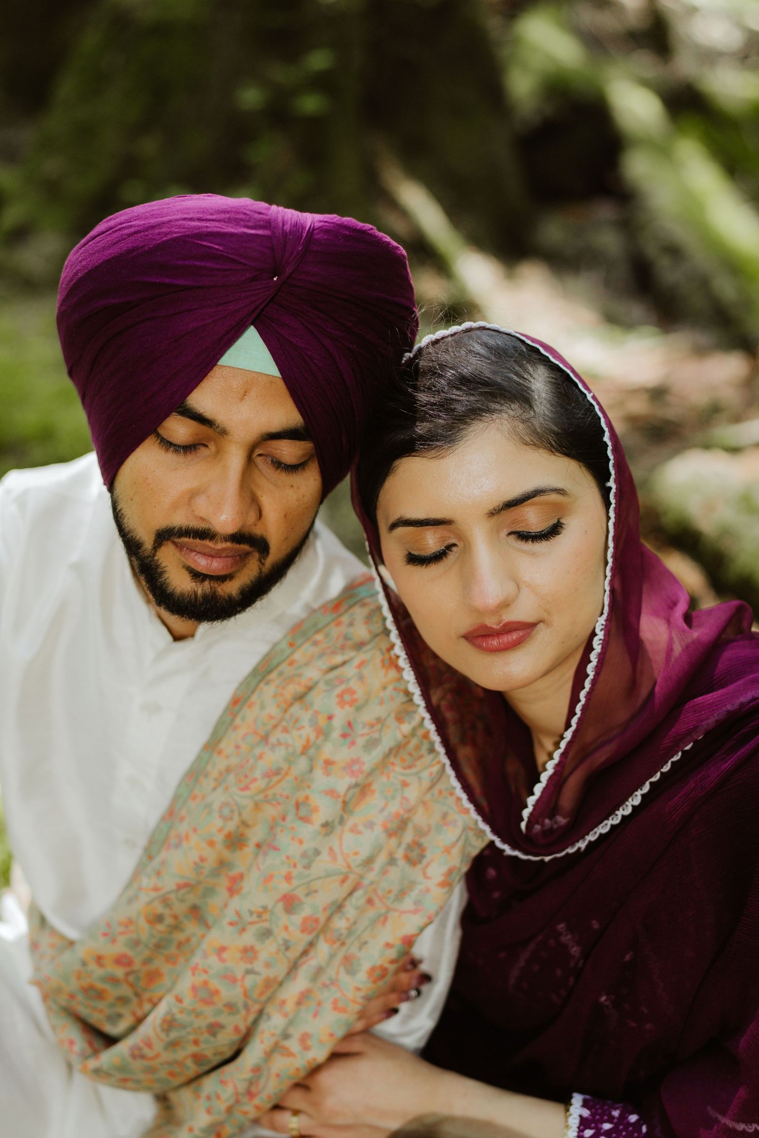 Close-up of Sikh couple in traditional attire, man in purple turban embracing woman in burgundy dupatta.