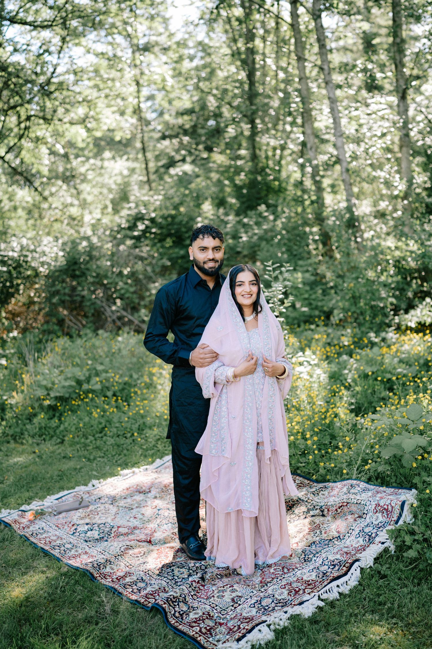 Couple sitting on decorative rug in a sunny woodland setting.