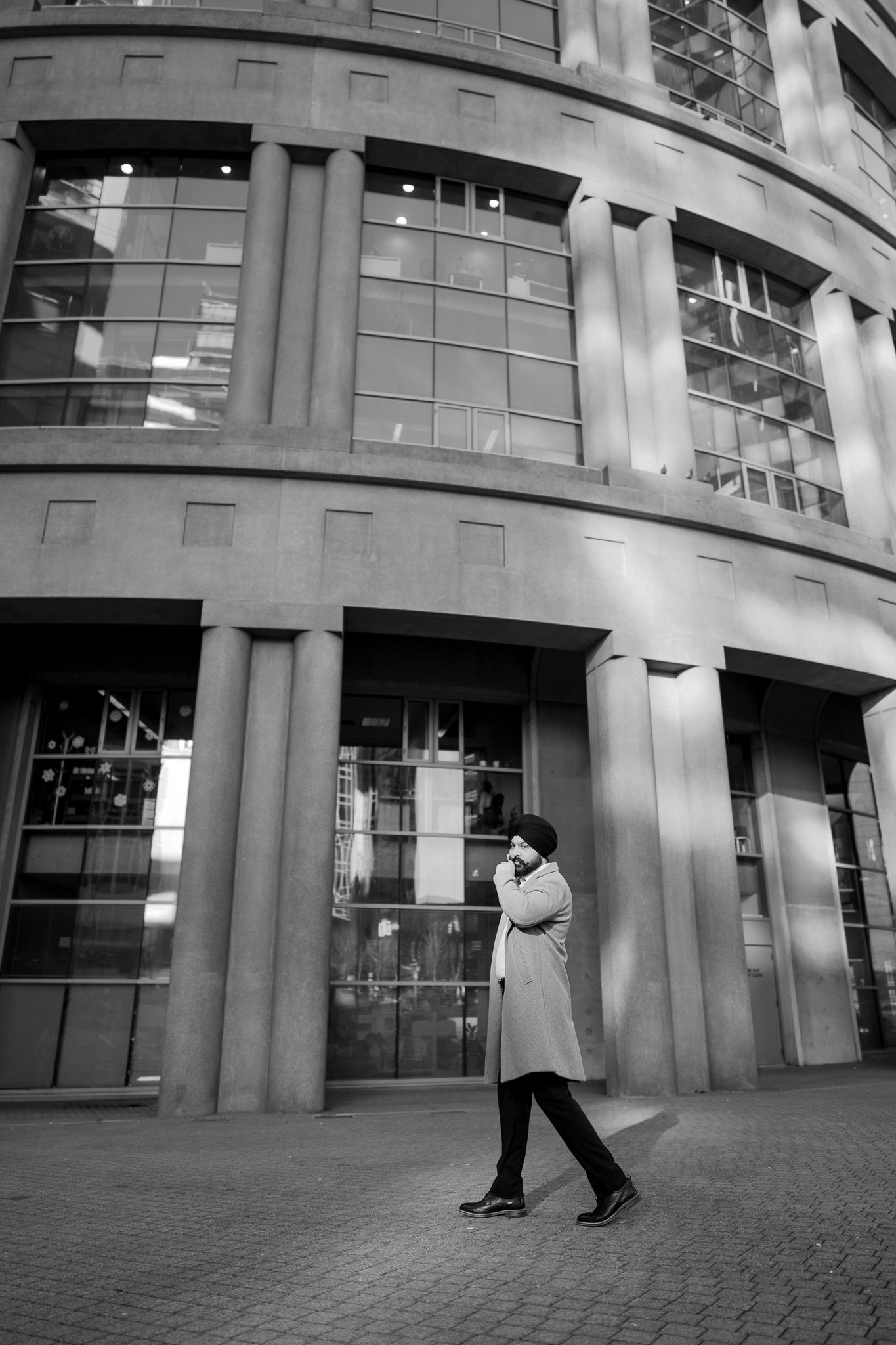 A black and white sequence of images showing a person in white clothing walking past a modern building's curved facade.