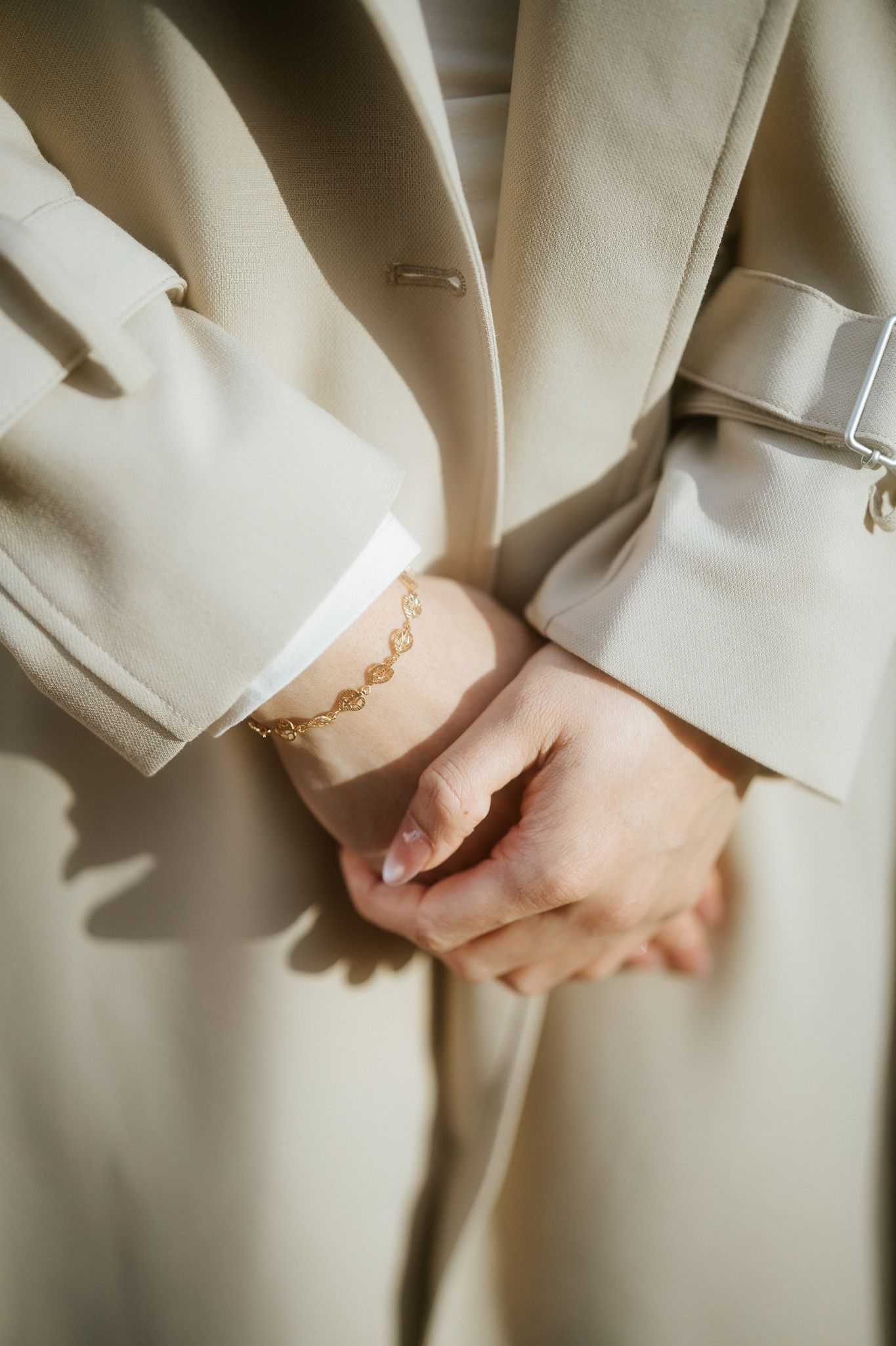 Close-up shots of hands wearing a delicate gold chain bracelet against a cream-colored sleeve background.