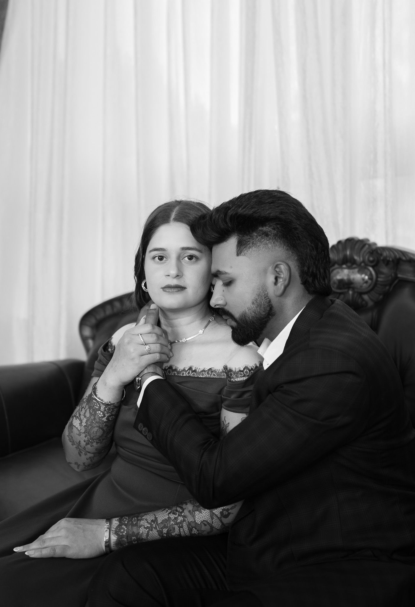 Romantic black and white portrait of couple sitting intimately on leather sofa.
