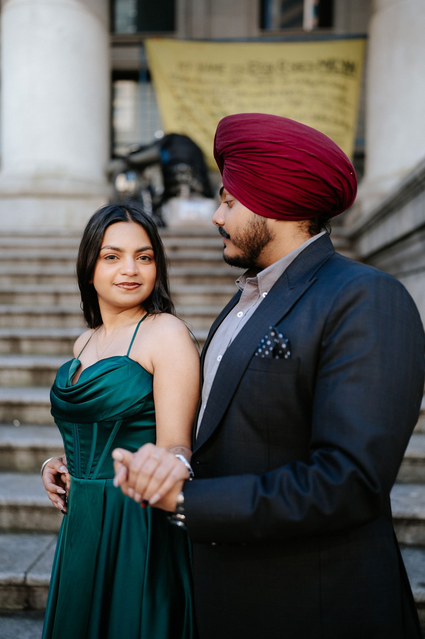 A romantic couple in formal attire share tender moments on stone steps, with her in an elegant emerald dress.