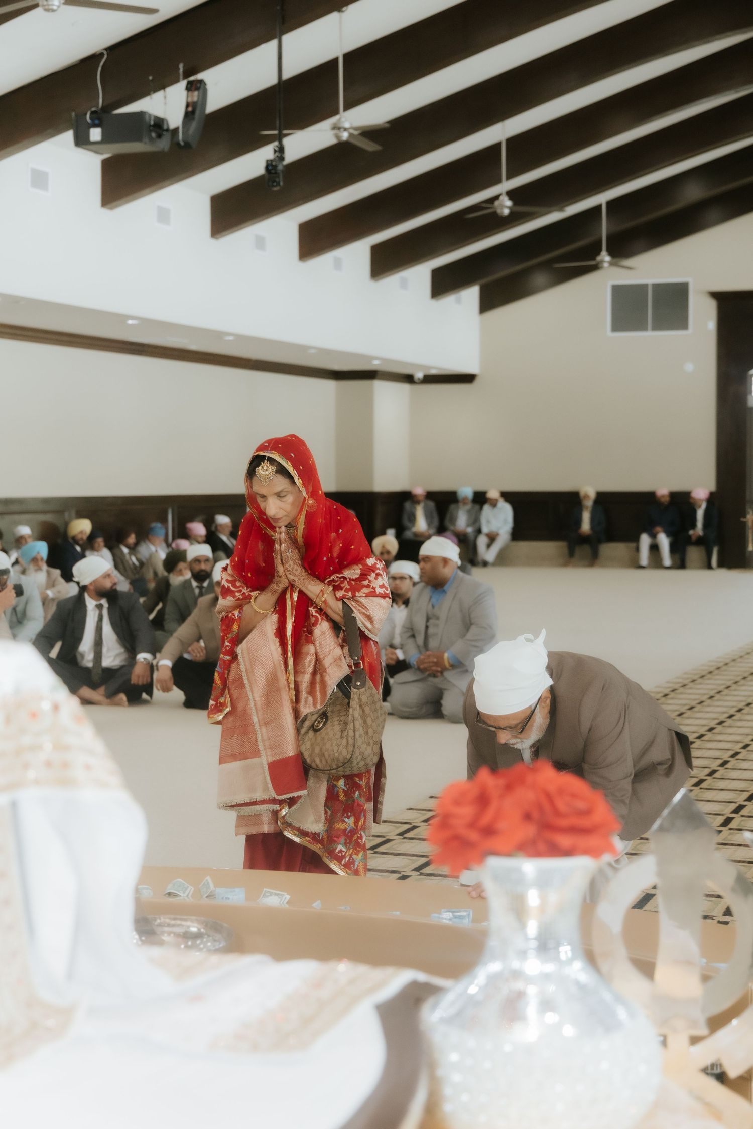 Sikh bride in red dupatta bowing during Anand Karaj wedding ceremony at Gurdwara.
