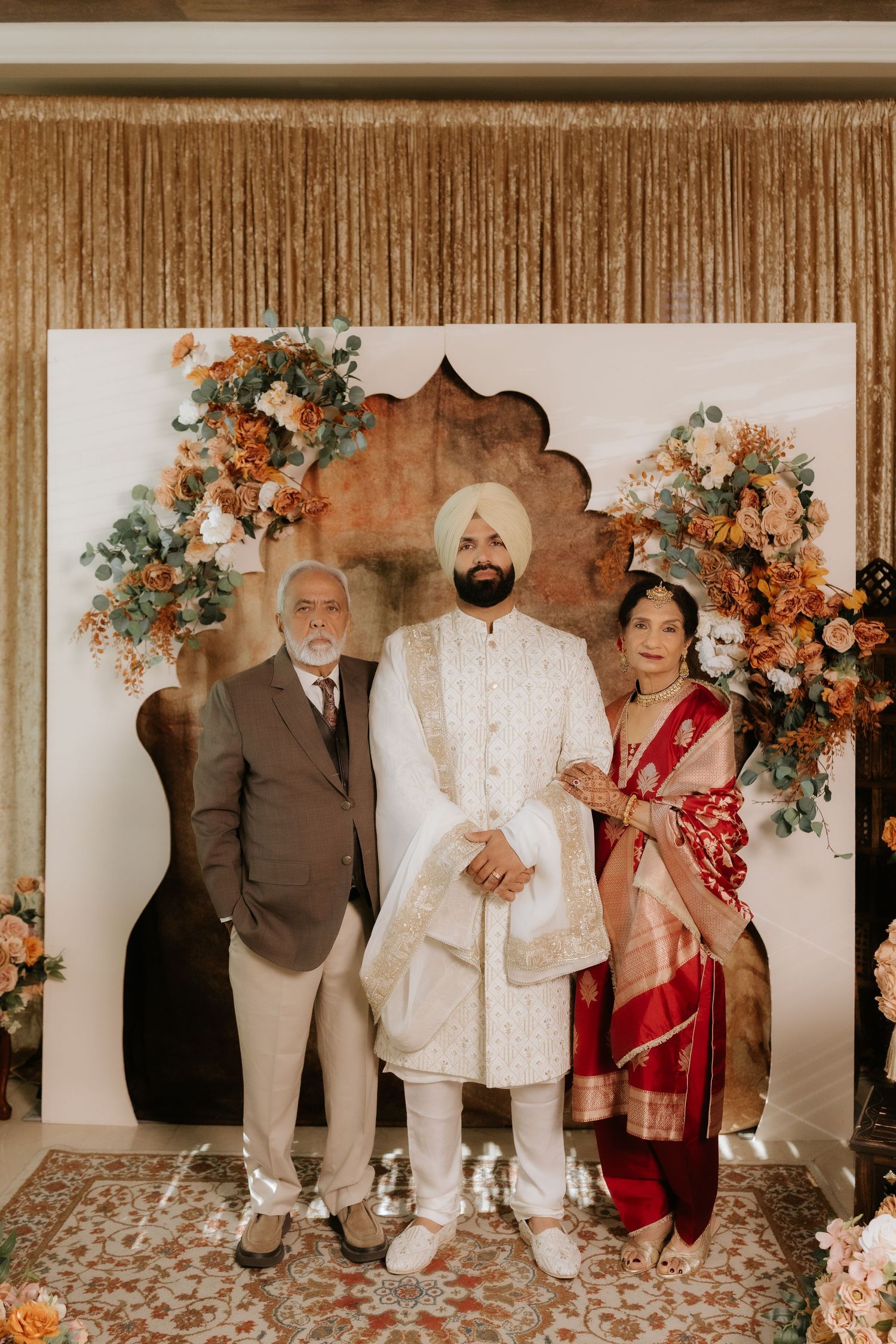 Sikh groom in white sherwani with turban poses with parents at traditional Indian wedding ceremony.
