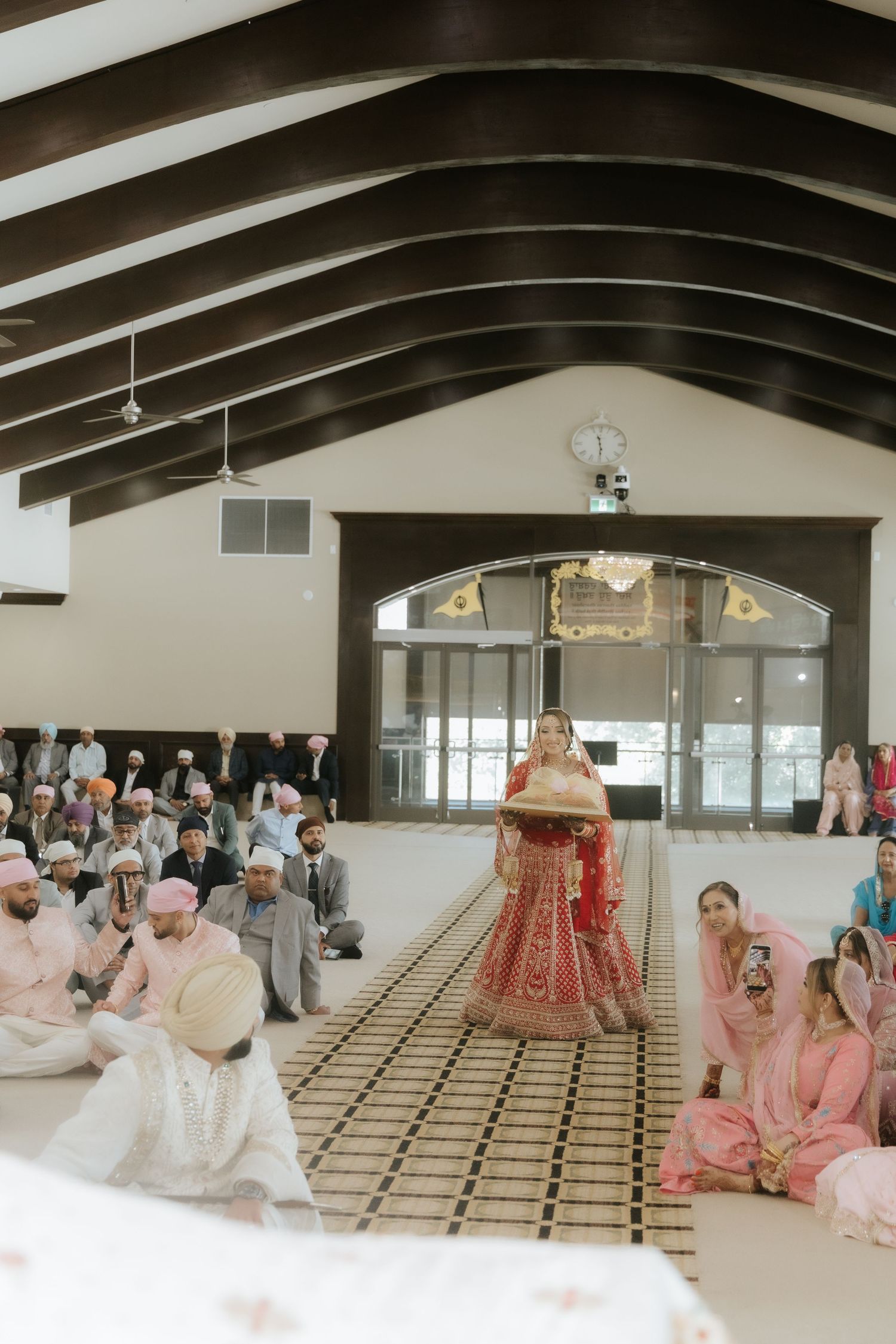 Sikh bride in red lehenga walks the aisle during Anand Karaj wedding ceremony in a gurudwara.
