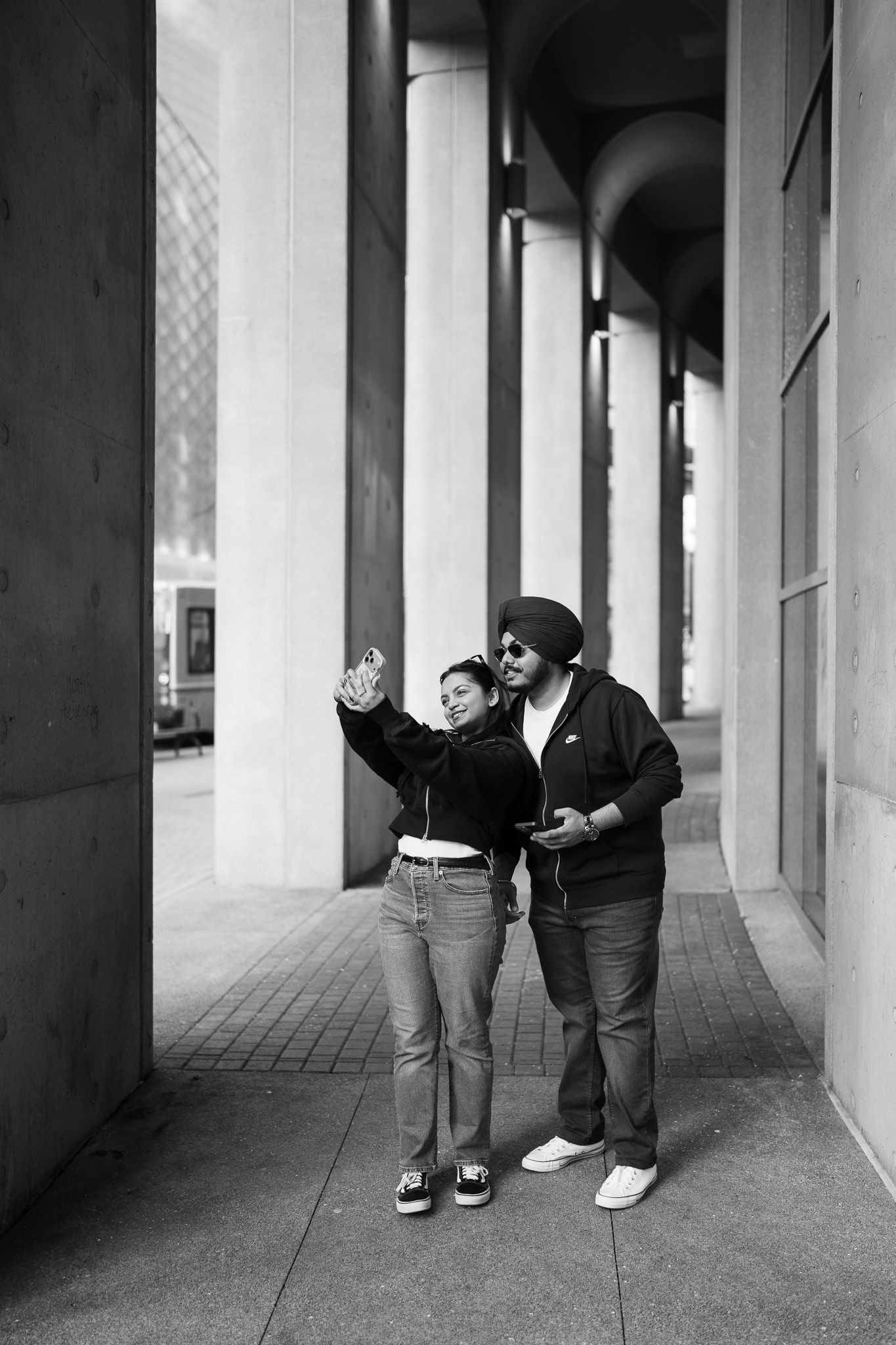 Two figures interact playfully in a minimalist architectural corridor with columns and natural lighting.