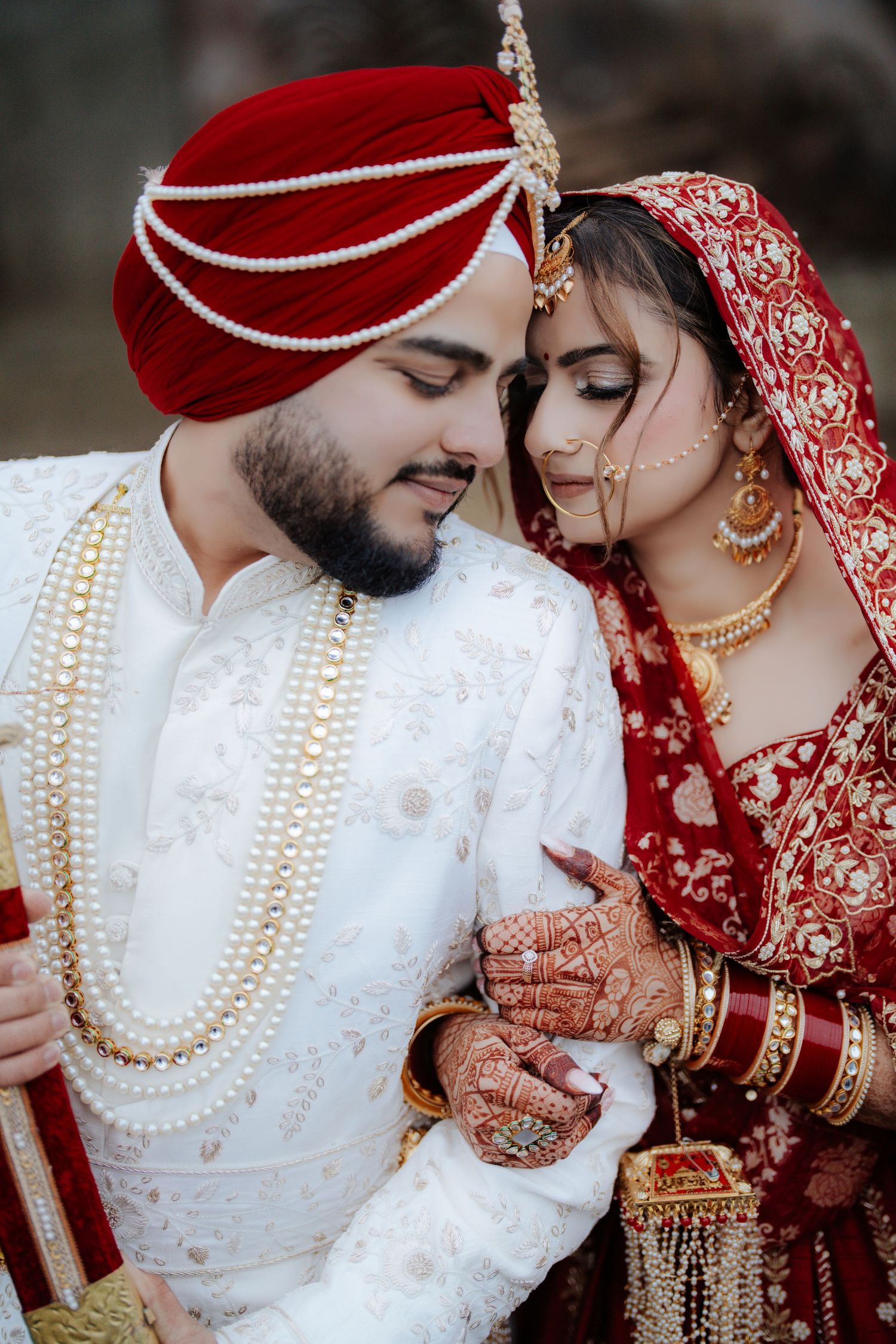 Close-up of traditional Indian wedding jewelry and attire in red and white with pearl necklaces.