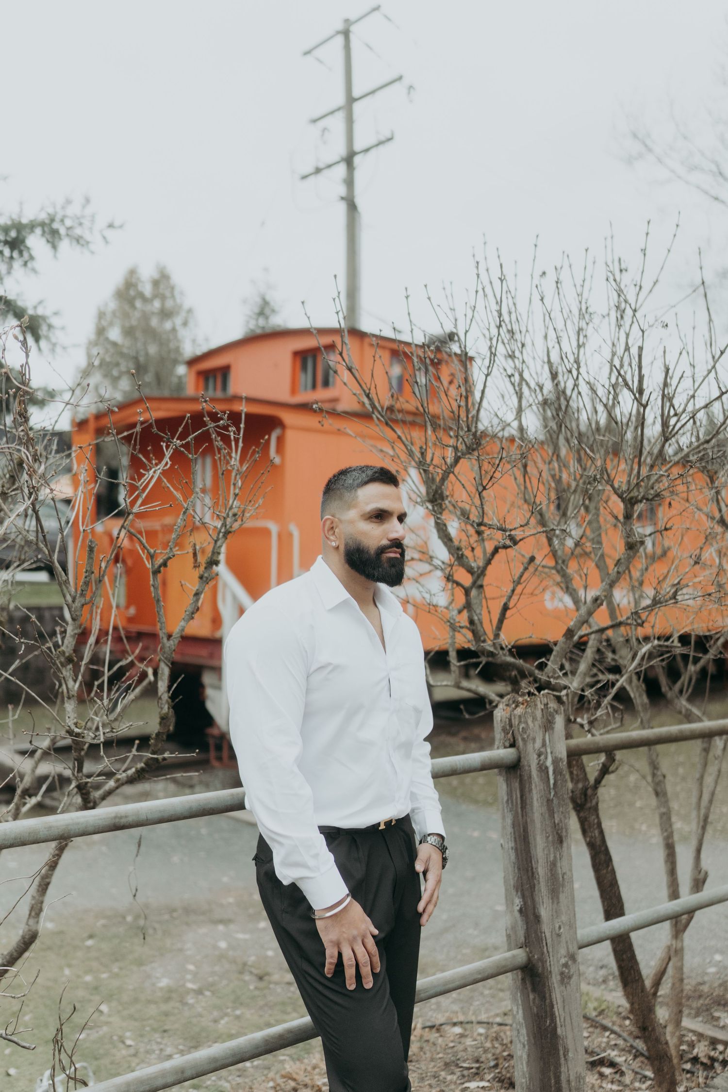 Person in white shirt poses near orange train car and bare winter trees.