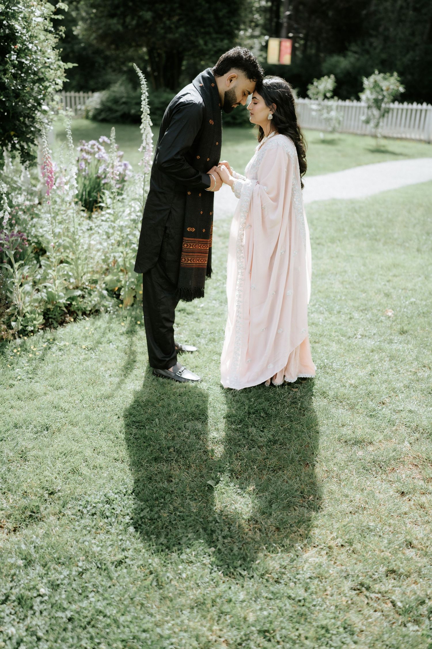 A couple shares a tender moment in a garden setting with pink flowers and greenery.