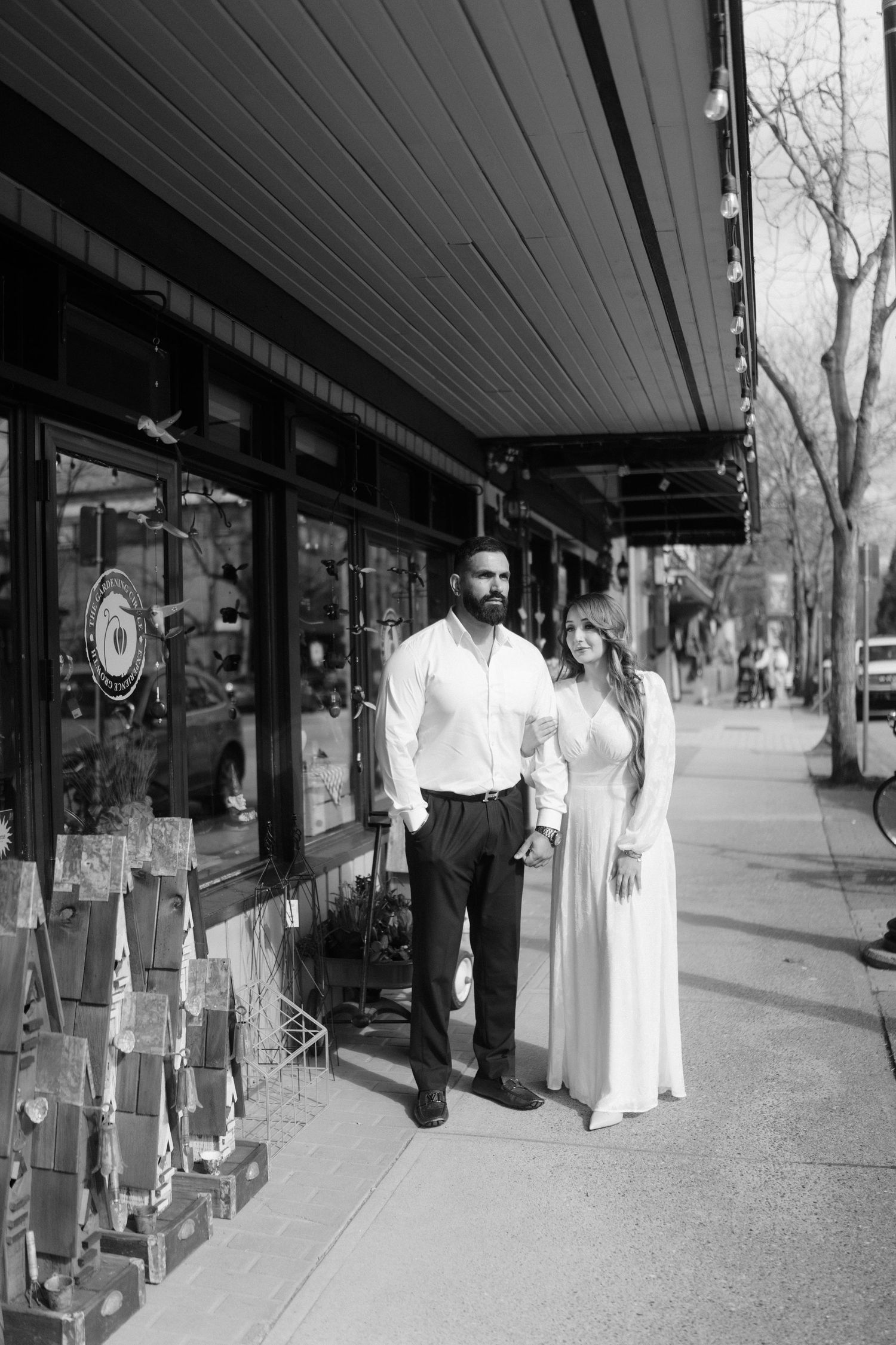 A black and white photo of a couple standing together outside a shop with window displays.
