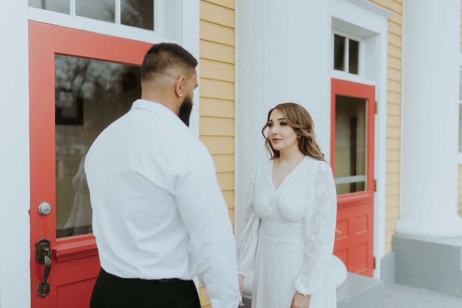Elegant white-clad figures against classical architecture with red doors.
