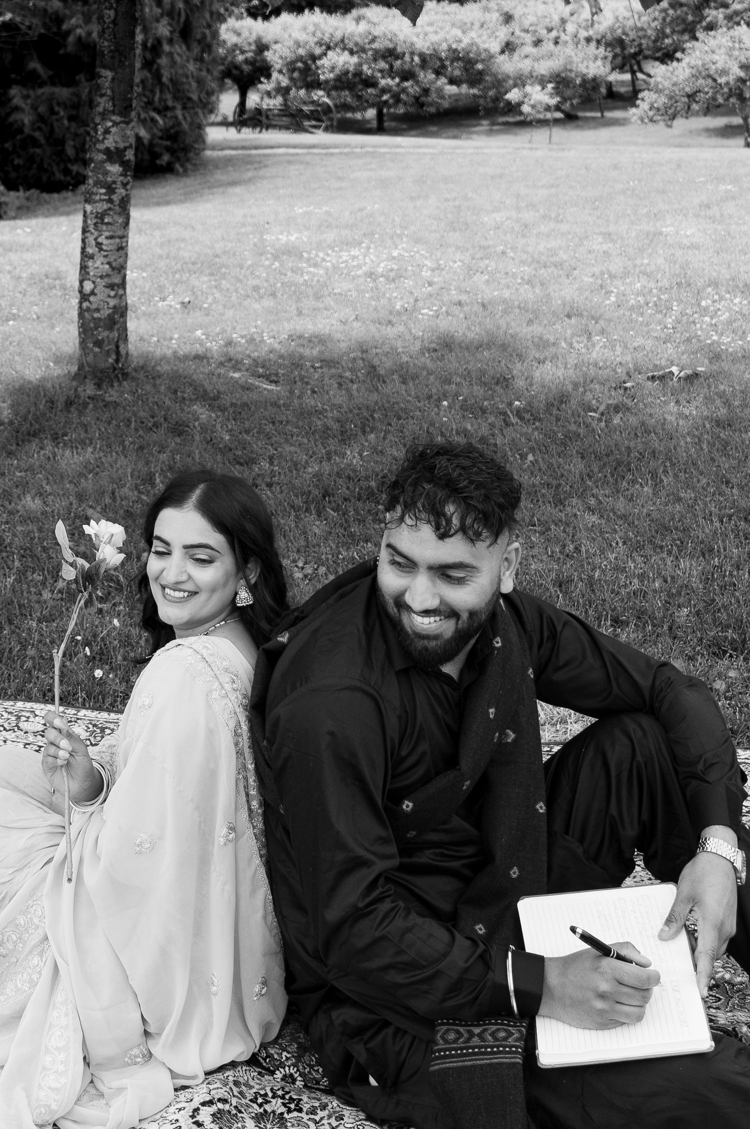 A black and white photo of a couple sharing a joyful moment on a blanket outdoors.