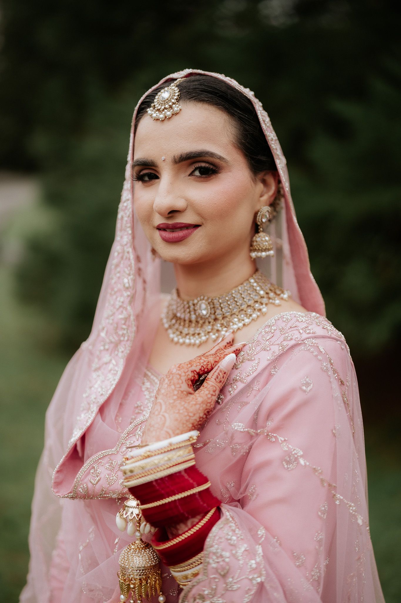 A bride in a pink embellished traditional outfit with ornate jewelry and veil poses in multiple close-up shots.