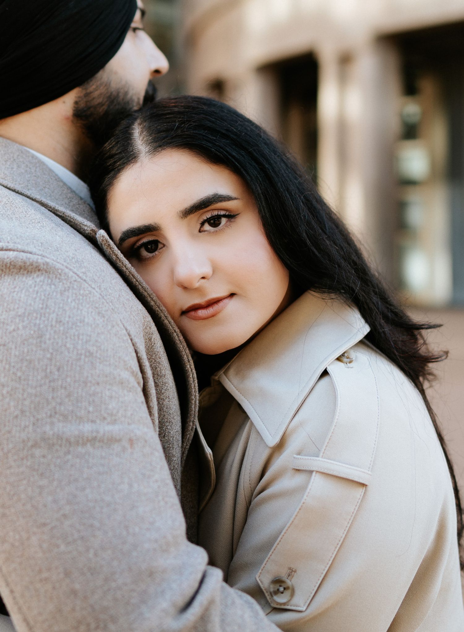 A romantic couple embraces in a soft, intimate photoshoot with muted tones and natural lighting.