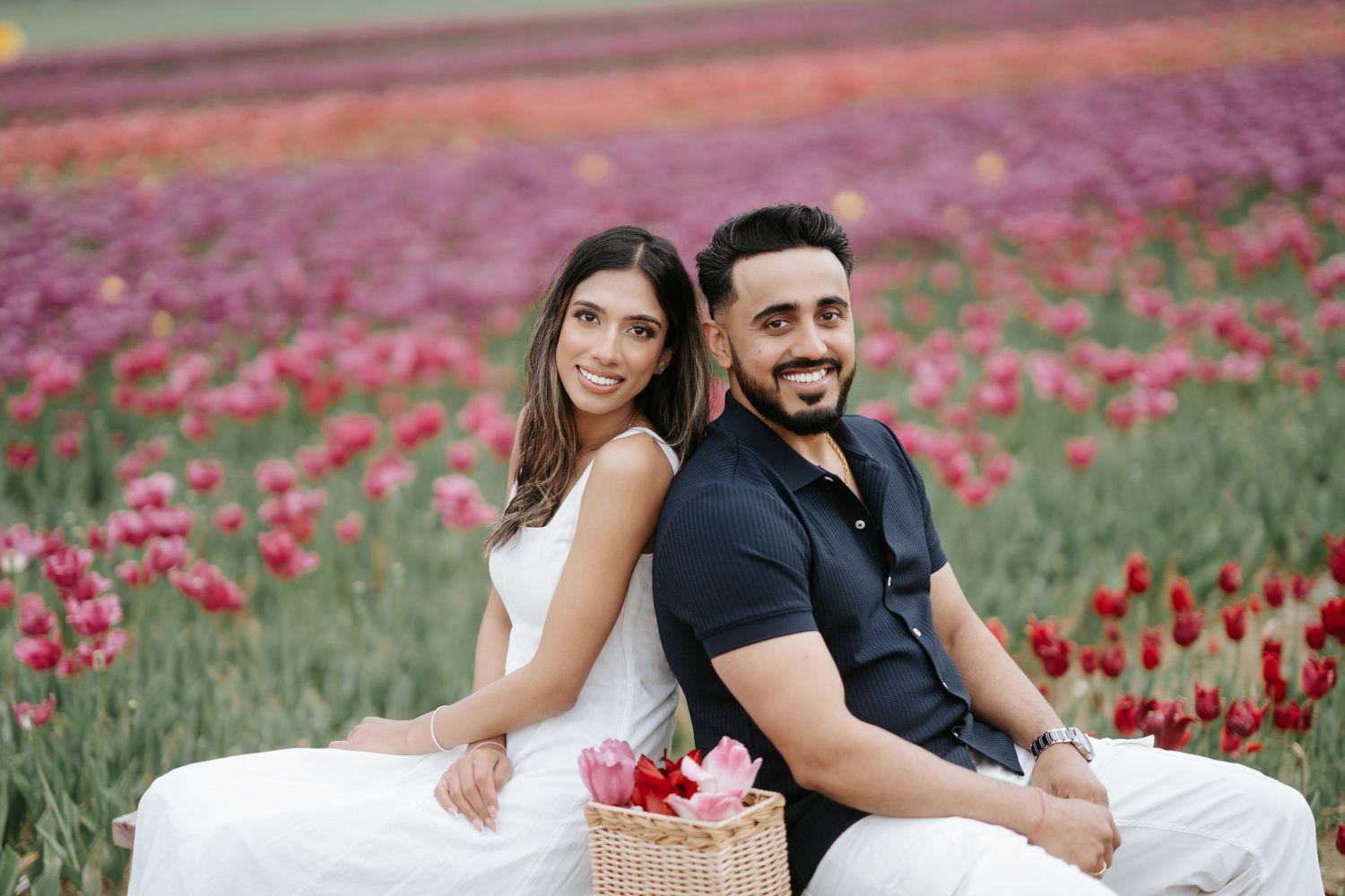 A couple poses together in a vibrant field of red tulips during a romantic spring photoshoot.