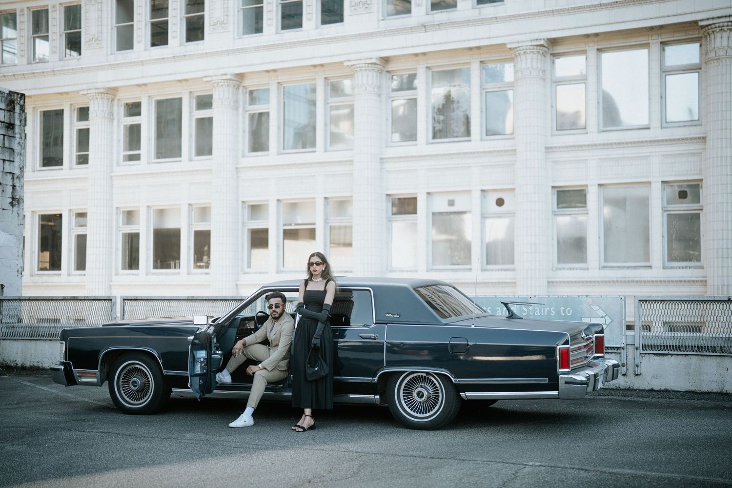 A vintage black and white Cadillac car parked in front of a large white building with multiple windows.